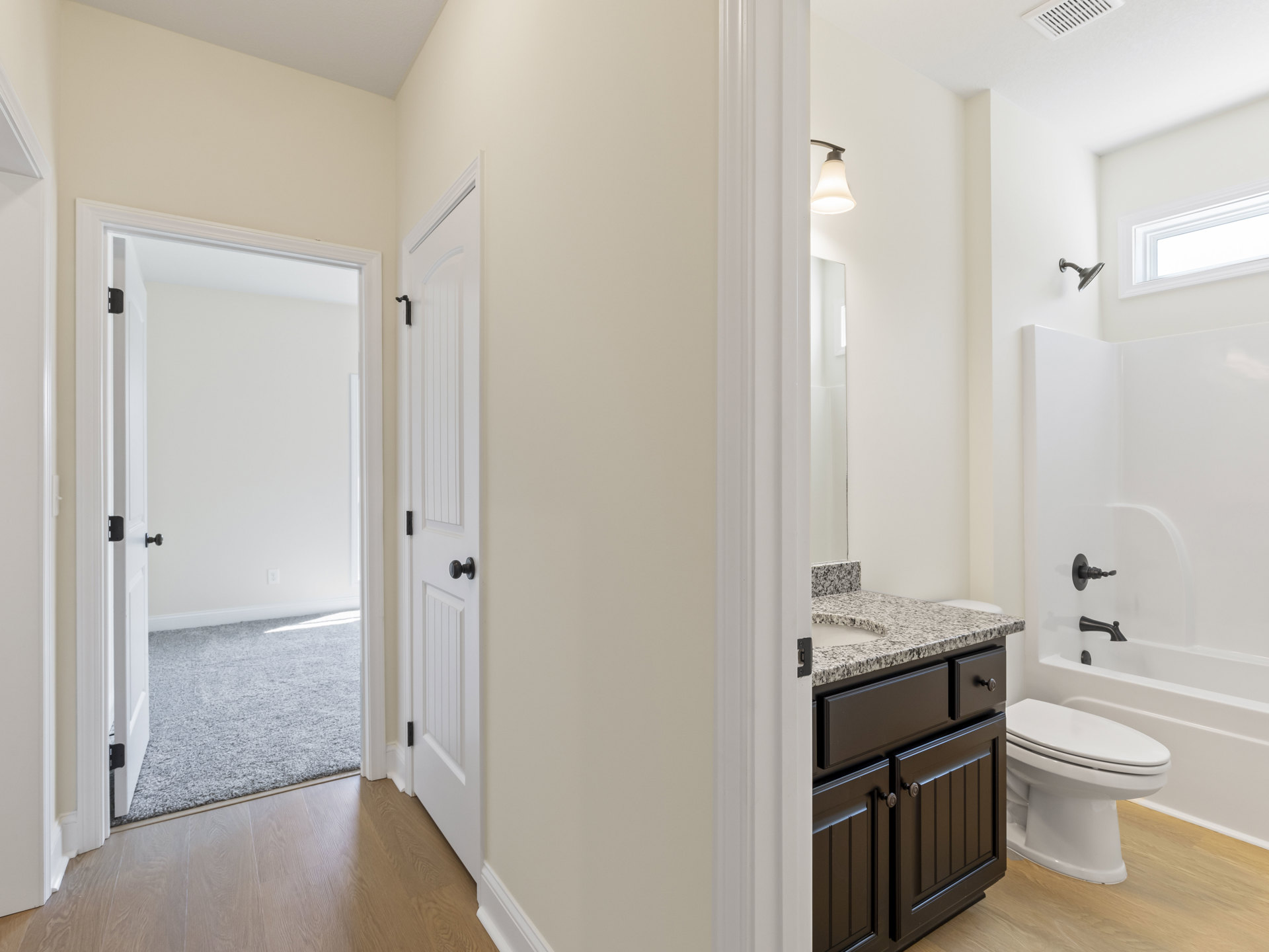 White bathroom with tile floor, white toilet, white vanity cabinet, undermount sink, black faucet, white door with black knob, and recessed ceiling light