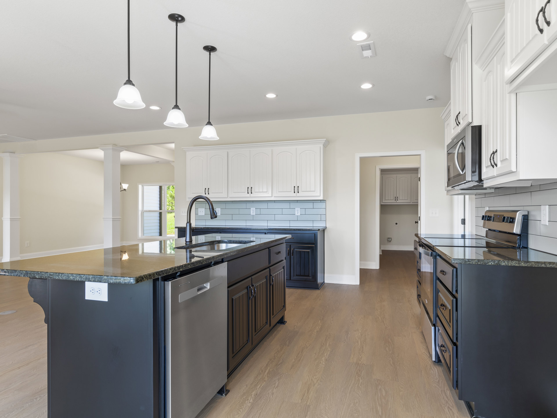 Modern kitchen featuring a central island with white quartz countertop, shaker-style cabinets in soft gray, stainless steel appliances including a built-in microwave and stove