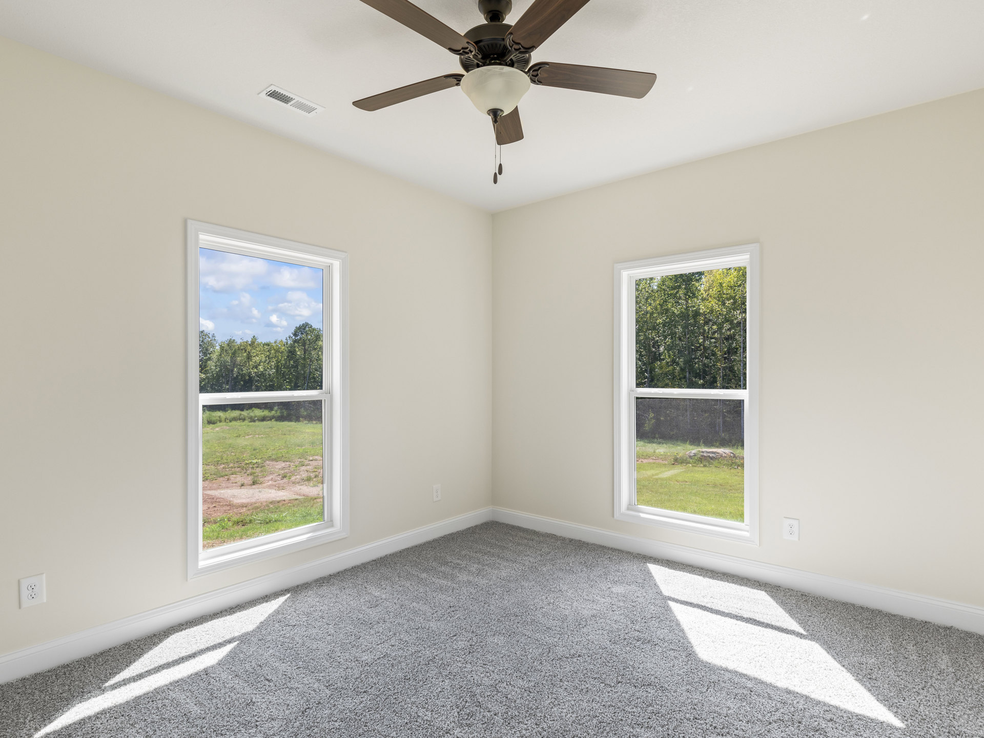 Neutral-toned carpeted room with plaster walls, ceiling fan and light fixture, large windows offering views of forest and open field