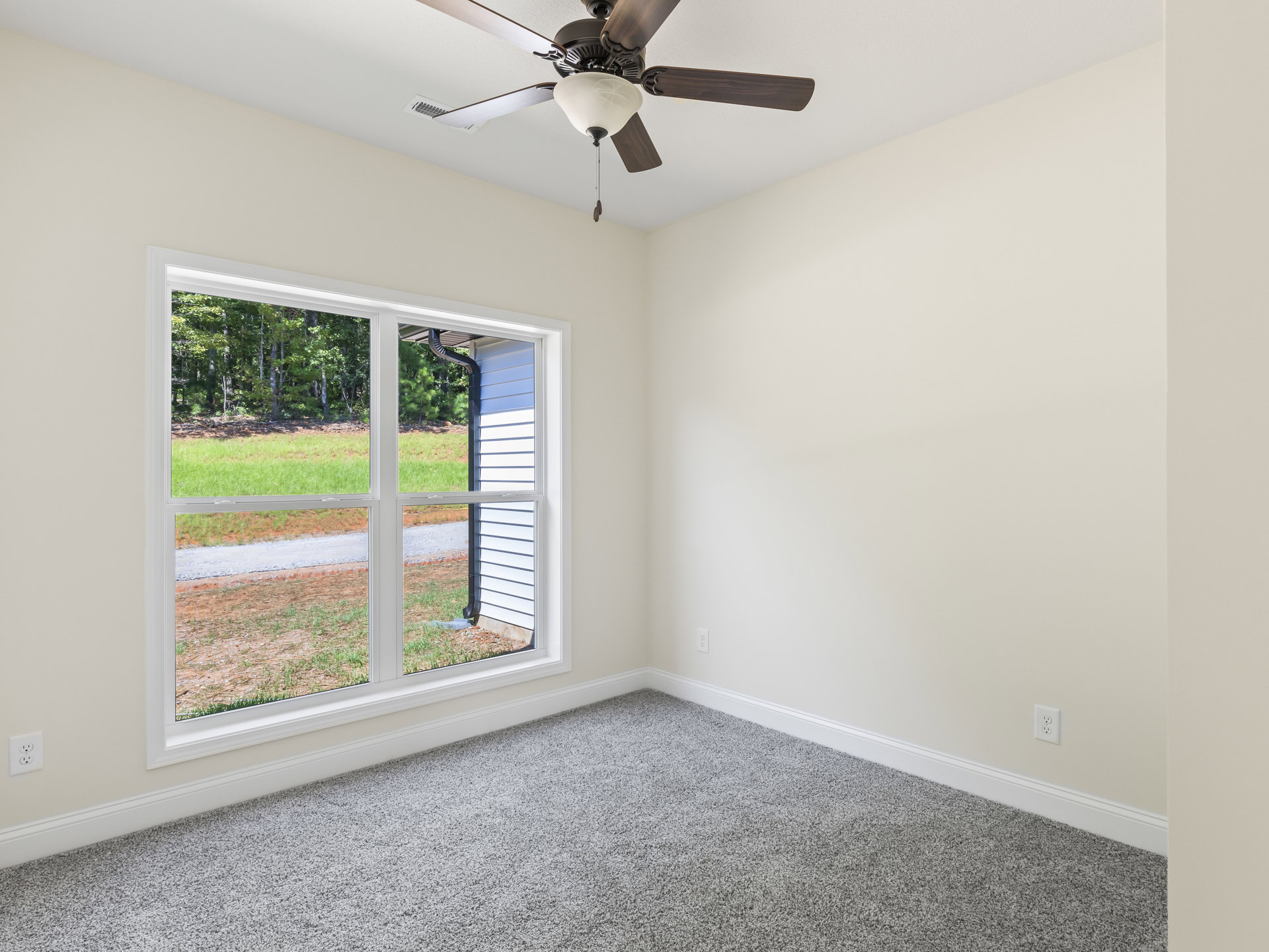 Carpeted room with white walls, ceiling fan with light fixture, window with blinds overlooking grassy field and neighboring house
