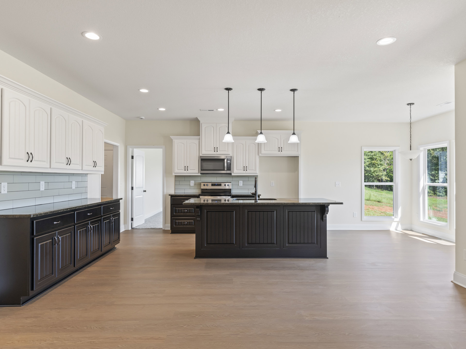 Kitchen and dining area featuring white cabinetry, black countertops, open microwave door, black kitchen island with drawers, window overlooking trees, white door with black knobs