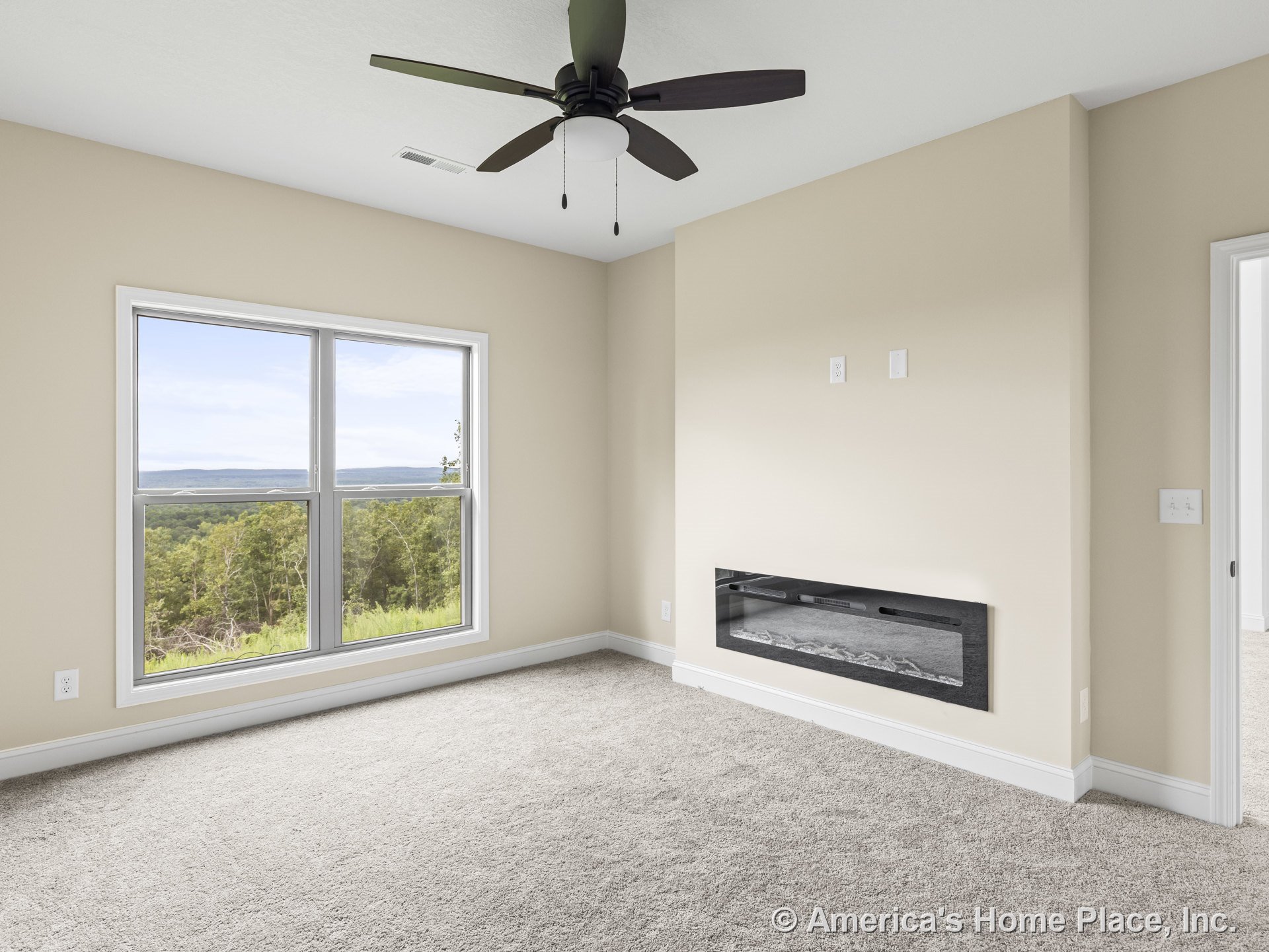 Spacious bedroom with large double window offering scenic views, wall-mounted electric fireplace, neutral carpet flooring, ceiling fan with built-in light, beige painted walls, and