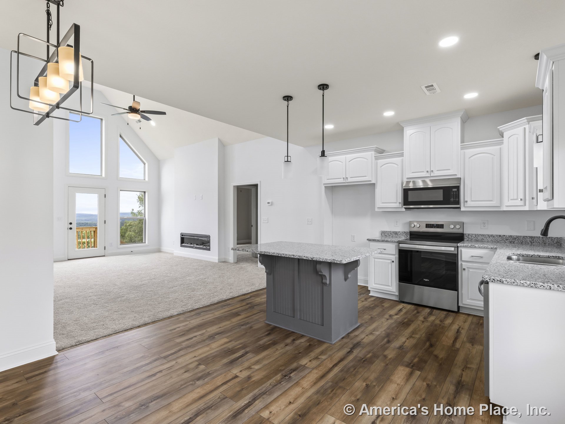 Open concept kitchen with white shaker cabinets, granite countertops, stainless steel appliances, and a central granite island, adjoining a vaulted living area with recessed