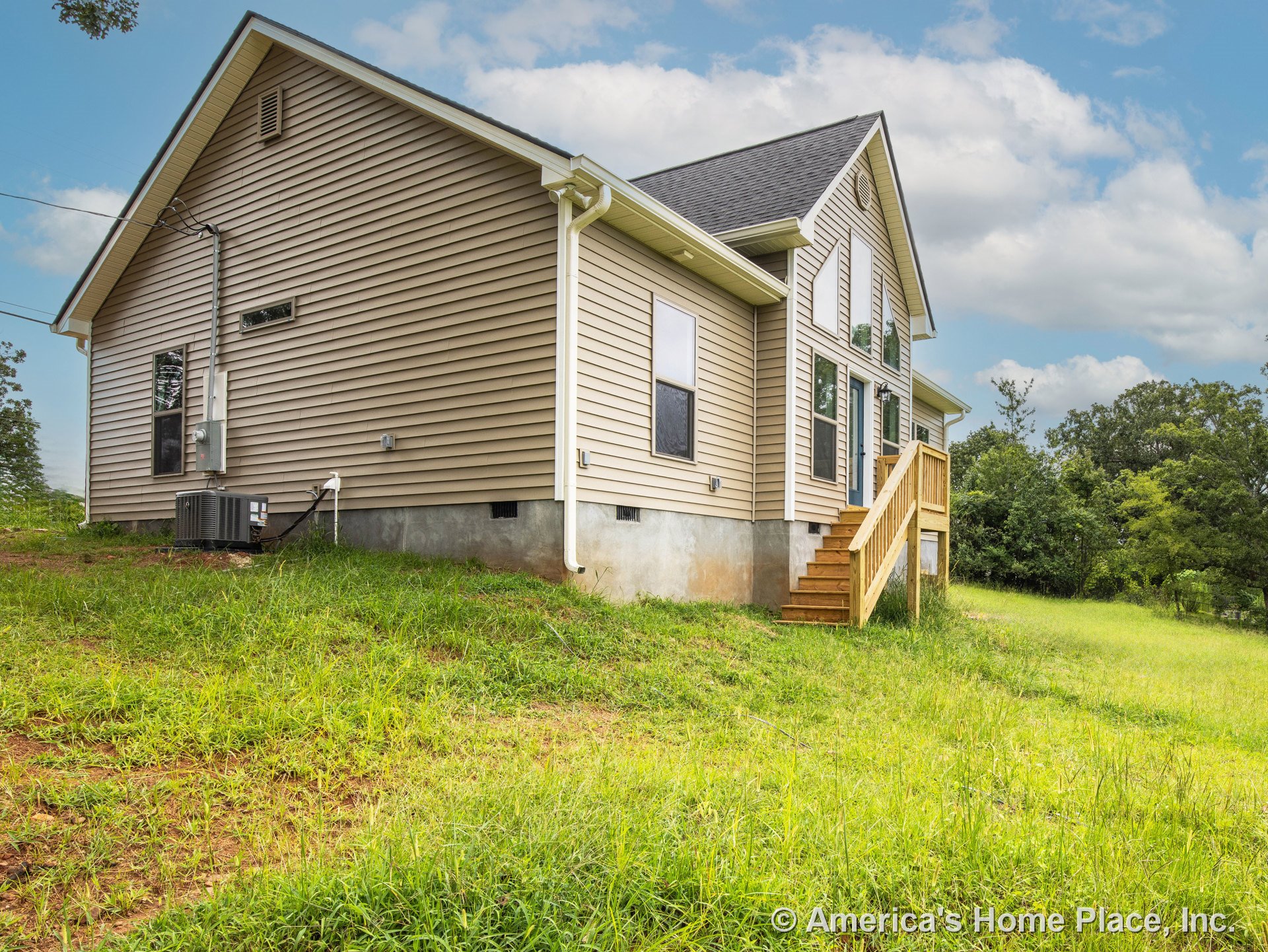 Beige vinyl siding exterior with gable roof, raised concrete foundation, wooden entry stairs and porch, multiple rectangular windows, white trim, exterior HVAC unit, and gutters.