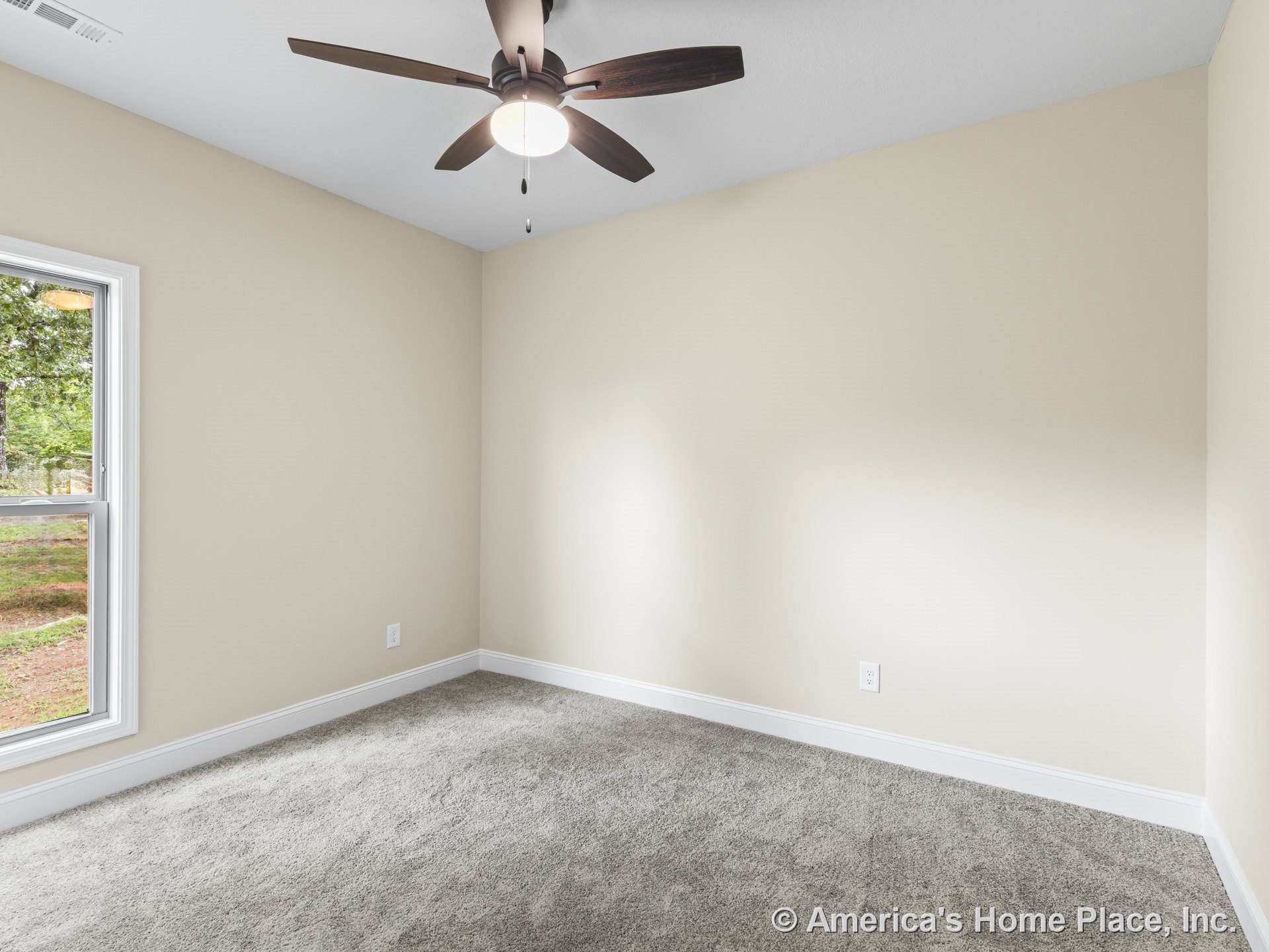 Bedroom with beige walls, gray carpet flooring, white baseboard trim, large window with white casing, ceiling fan and light fixture on flat white ceiling, modern neutral finishes.