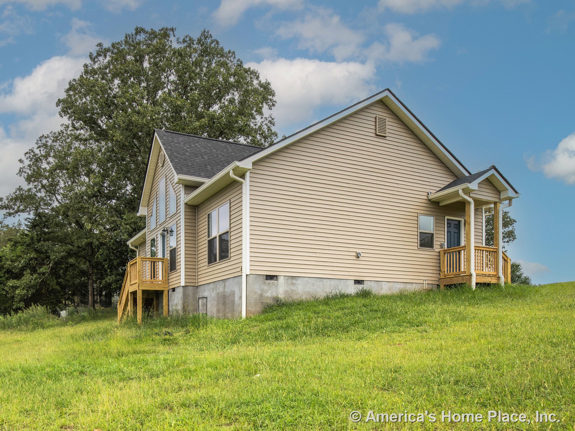 Beige vinyl siding exterior with gable roof covered in asphalt shingles, two wooden porches with railings, concrete foundation, multiple double-hung windows, white trim and