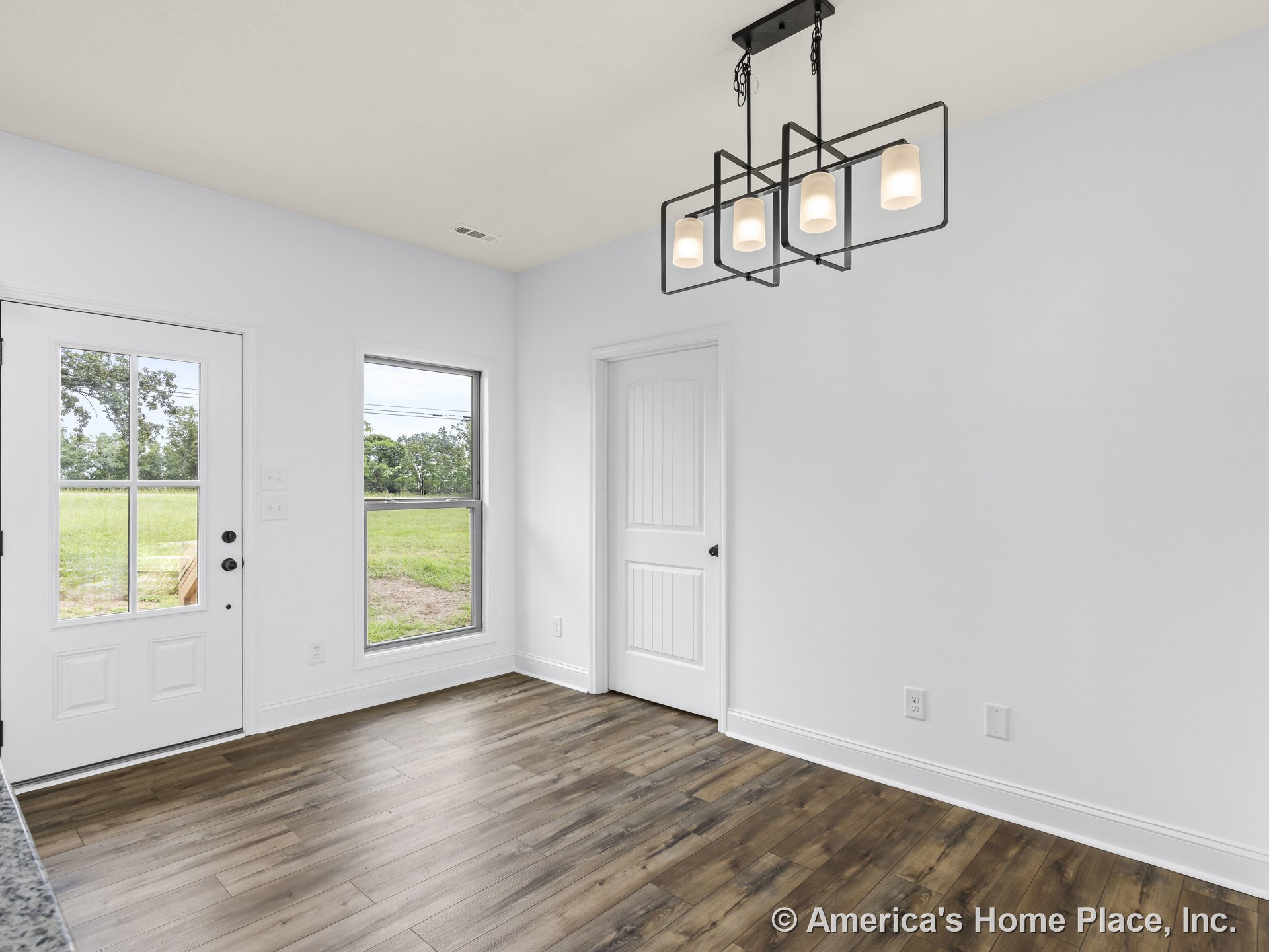 Dining area with wood-look plank flooring, modern geometric chandelier, white trim and baseboards, large window providing natural light, white paneled interior door, and exterior