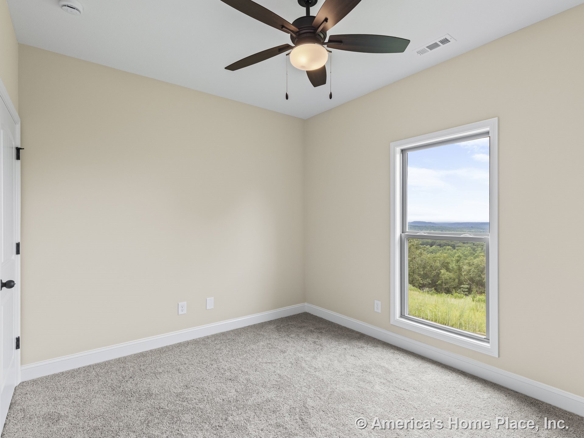 Bedroom with large white-trimmed window, beige painted walls, ceiling fan with integrated light, gray carpet flooring, white baseboards, and white paneled door.