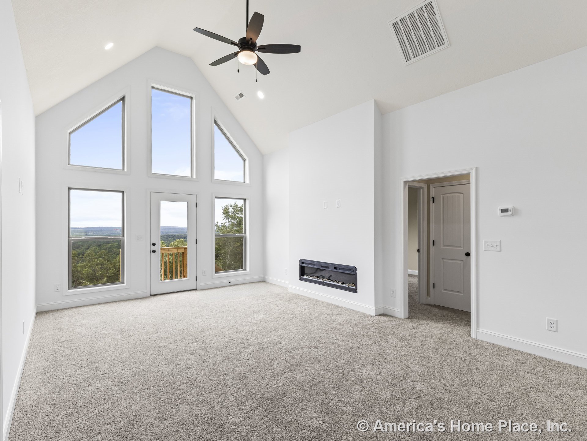 Vaulted ceiling with recessed lighting, expansive triangular windows allowing natural light, modern wall-mounted electric fireplace, neutral carpet flooring, white trim and
