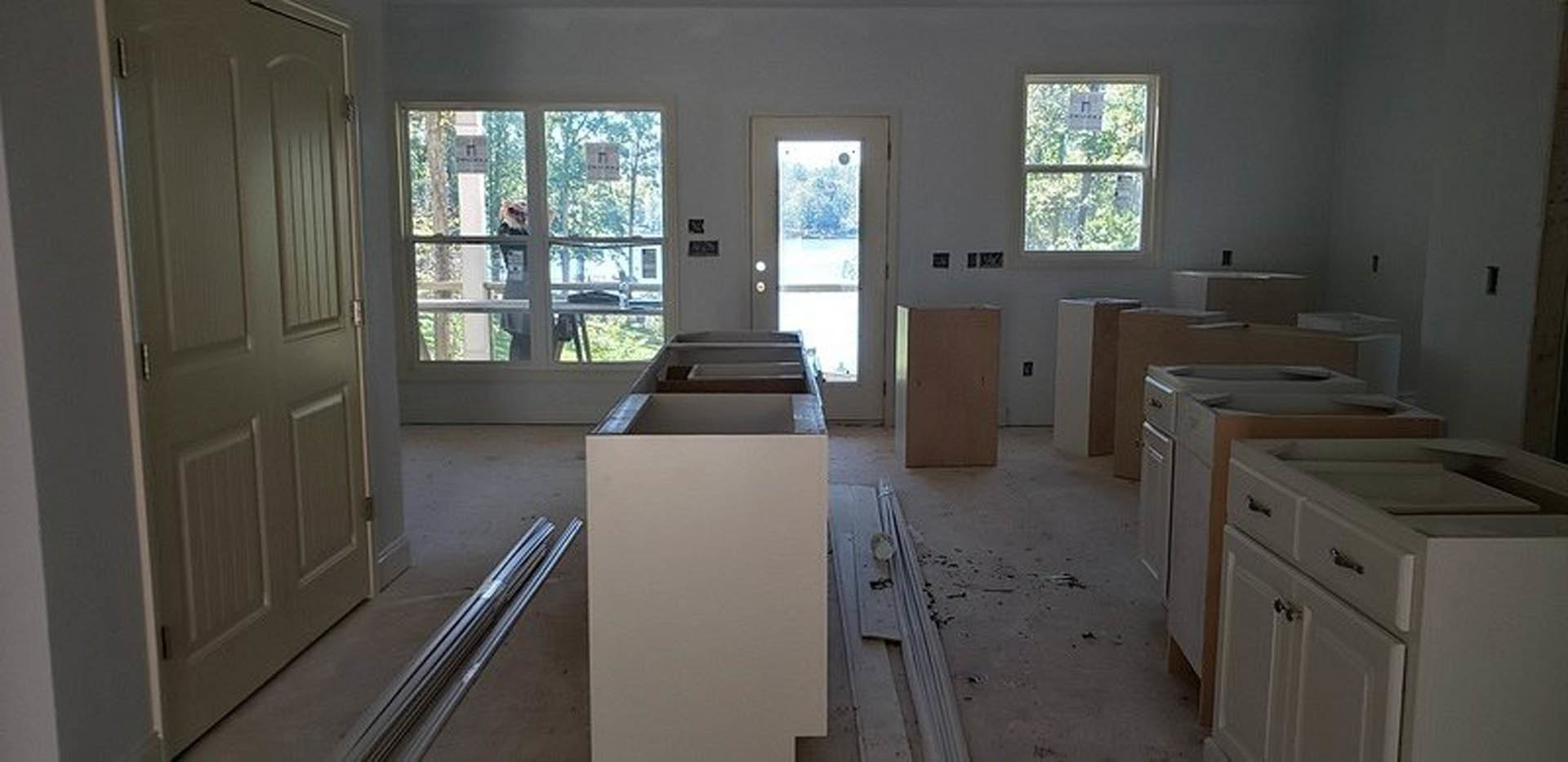Modern kitchen featuring white cabinets with drawers, stainless steel sink, black countertop, brown door with metal frame, and window displaying a sign.