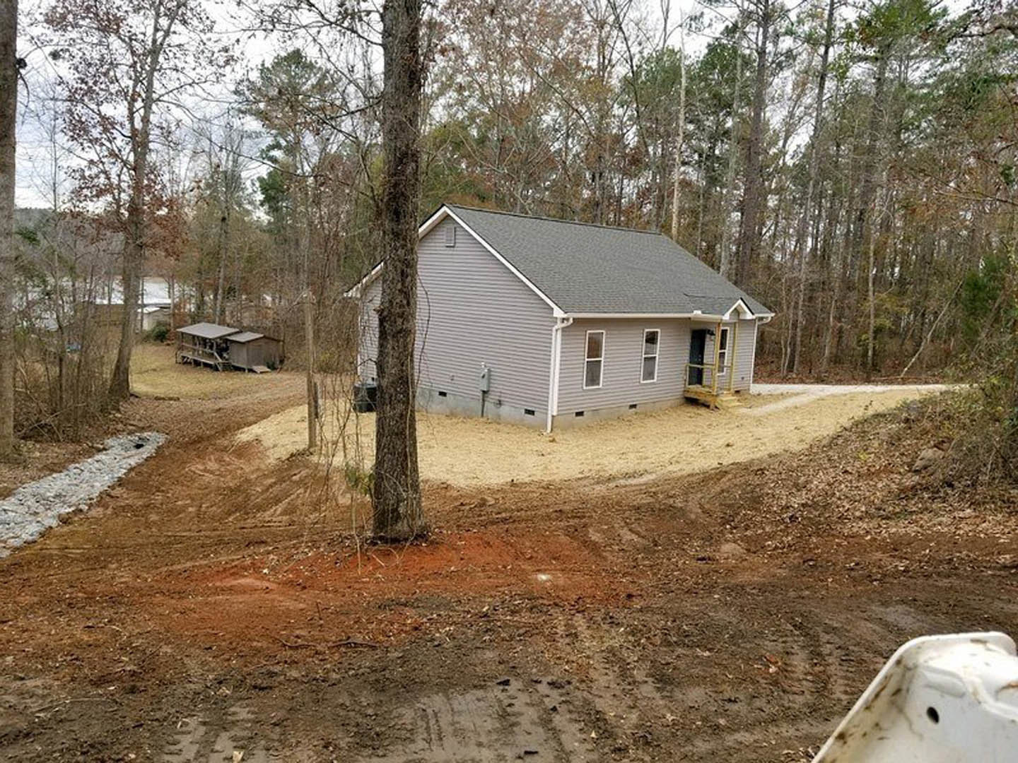 Grey wood-sided home with white trim nestled among tall trees, stone pathway leading to front entrance, grassy yard, and natural landscaping.
