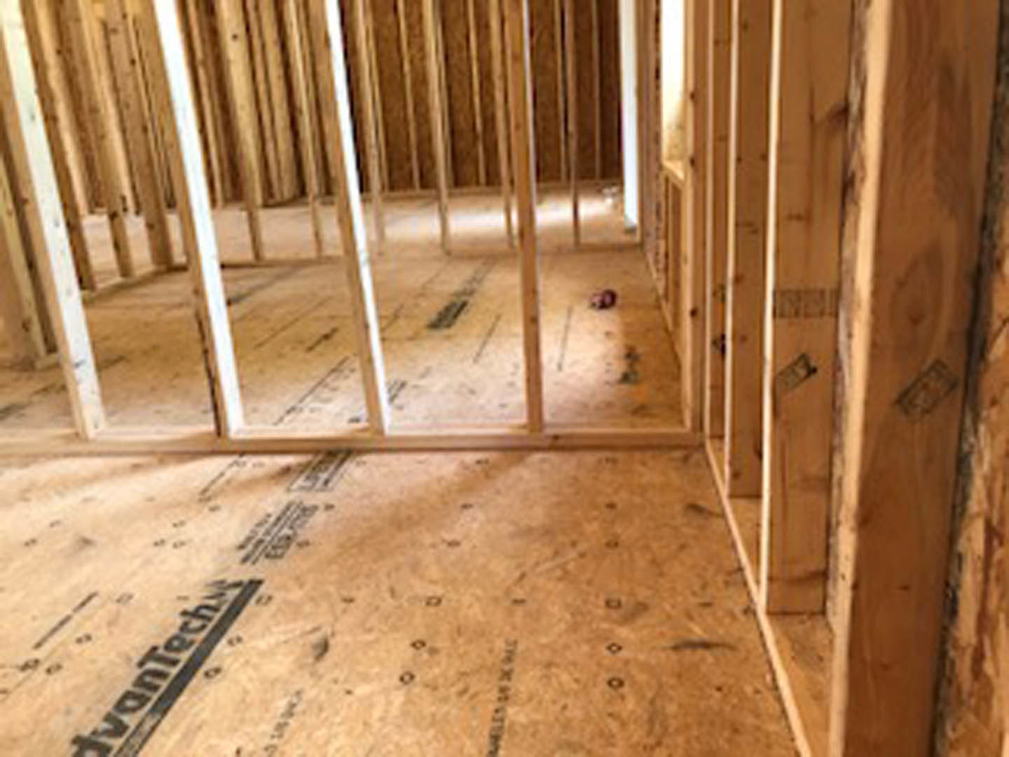 Exposed wood framing and beams in an unfinished room with plywood flooring and hardwood planks
