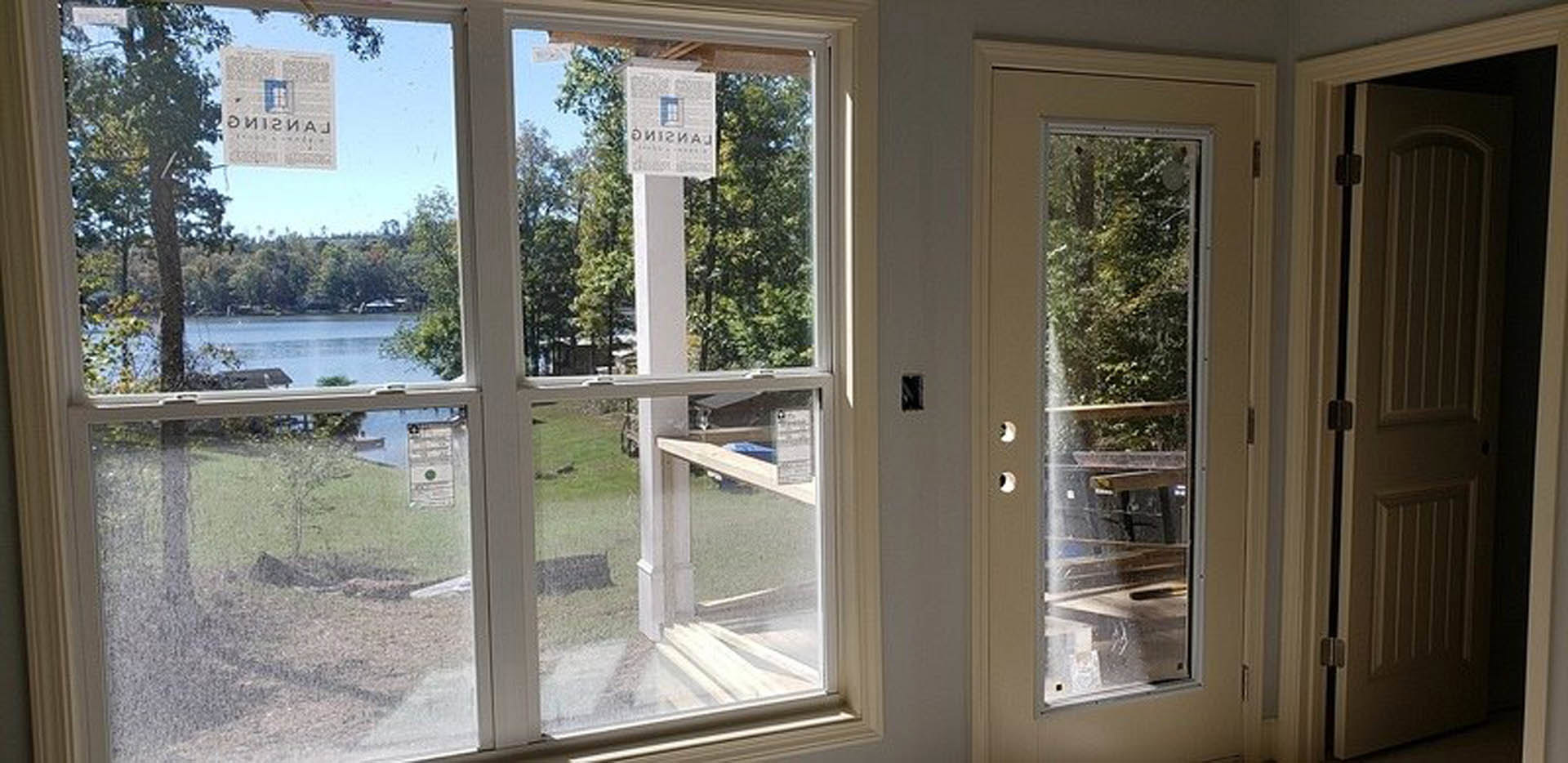 White-framed door and window set in a beige stucco wall, with a glimpse of hardwood flooring inside and leafy tree branches outside
