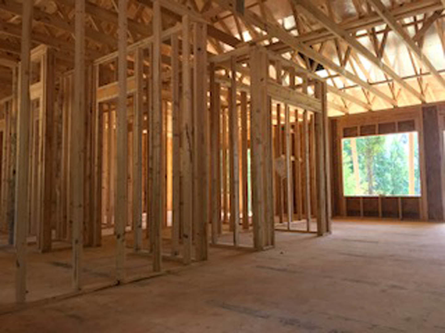 Exposed wood framing and beams in an unfinished room with a partially visible window and blurred figure in the background