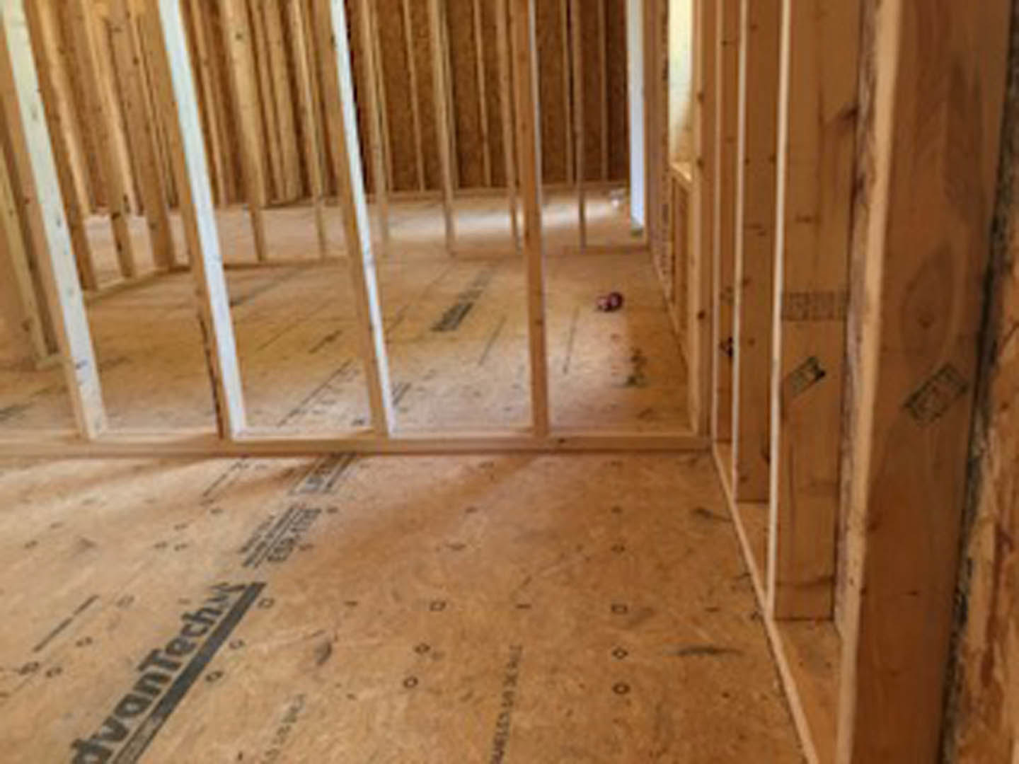 Unfinished room with exposed wood framing, plywood subfloor, visible wall outlet, and building insulation