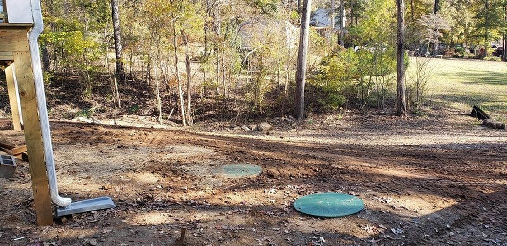Cluster of round stones on bare dirt beside a wooden post with a white pole, surrounded by sparse grass and plants in an outdoor residential yard