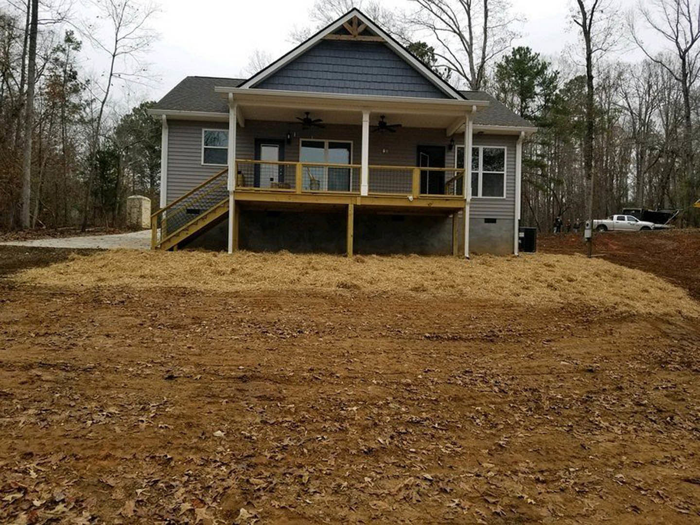 Spacious covered porch with ceiling fan, stone pillar, white-framed windows, and dirt yard scattered with brown leaves