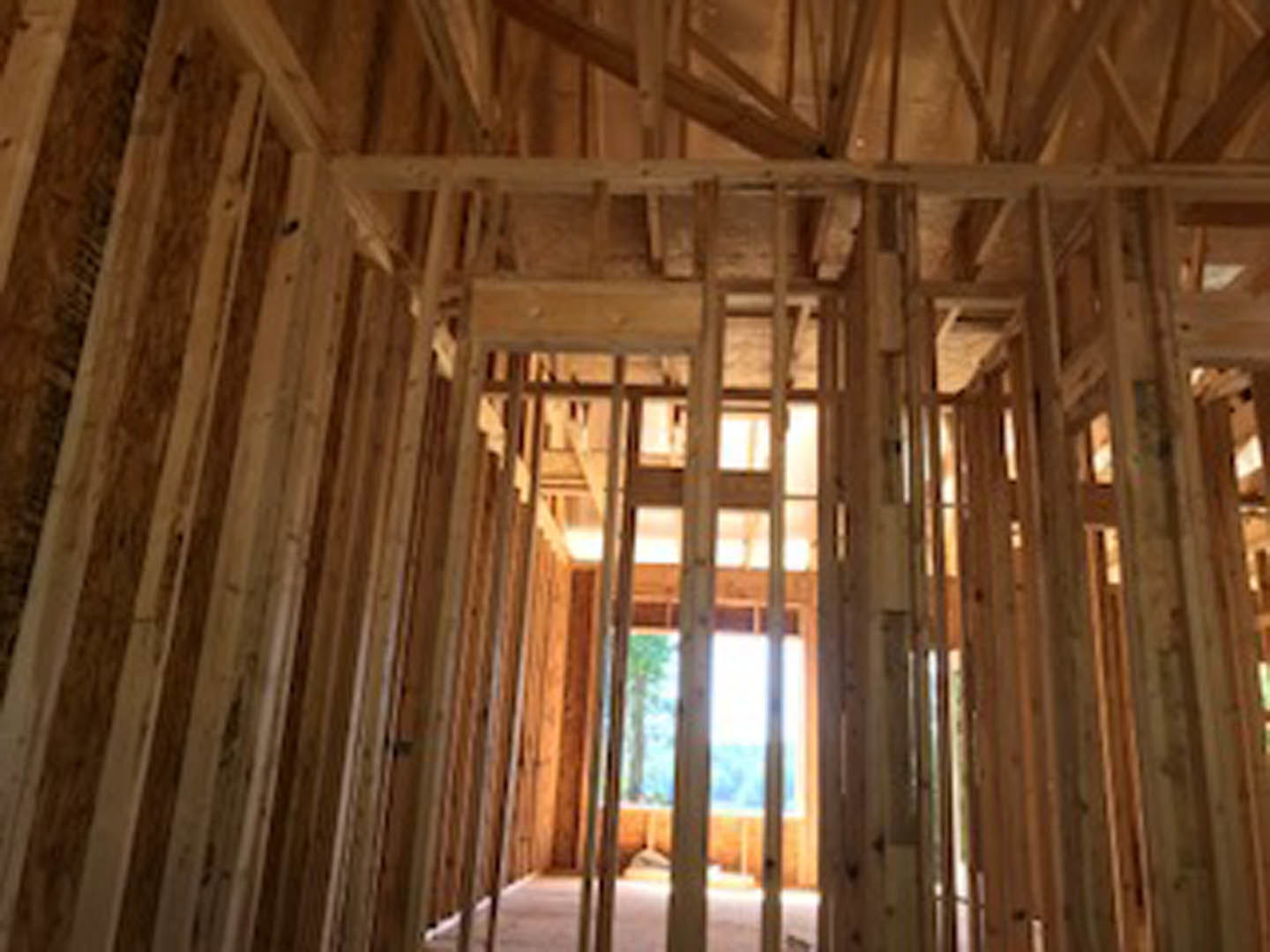 Exposed wood framing and beams inside a partially constructed home, with visible window opening and building insulation