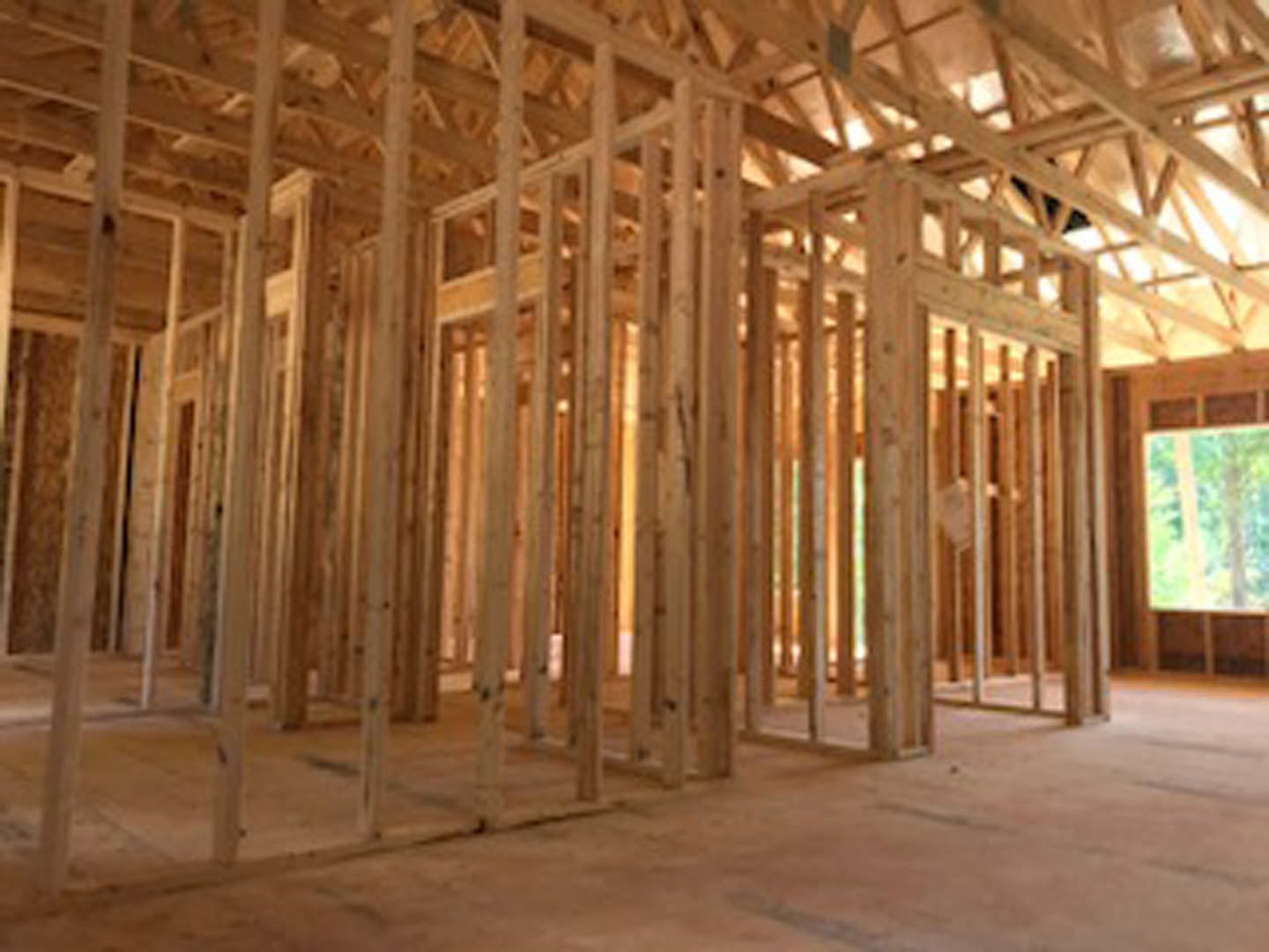 Exposed wooden framing and beams with insulation in progress, unfinished floors and ceiling inside a residential home under construction