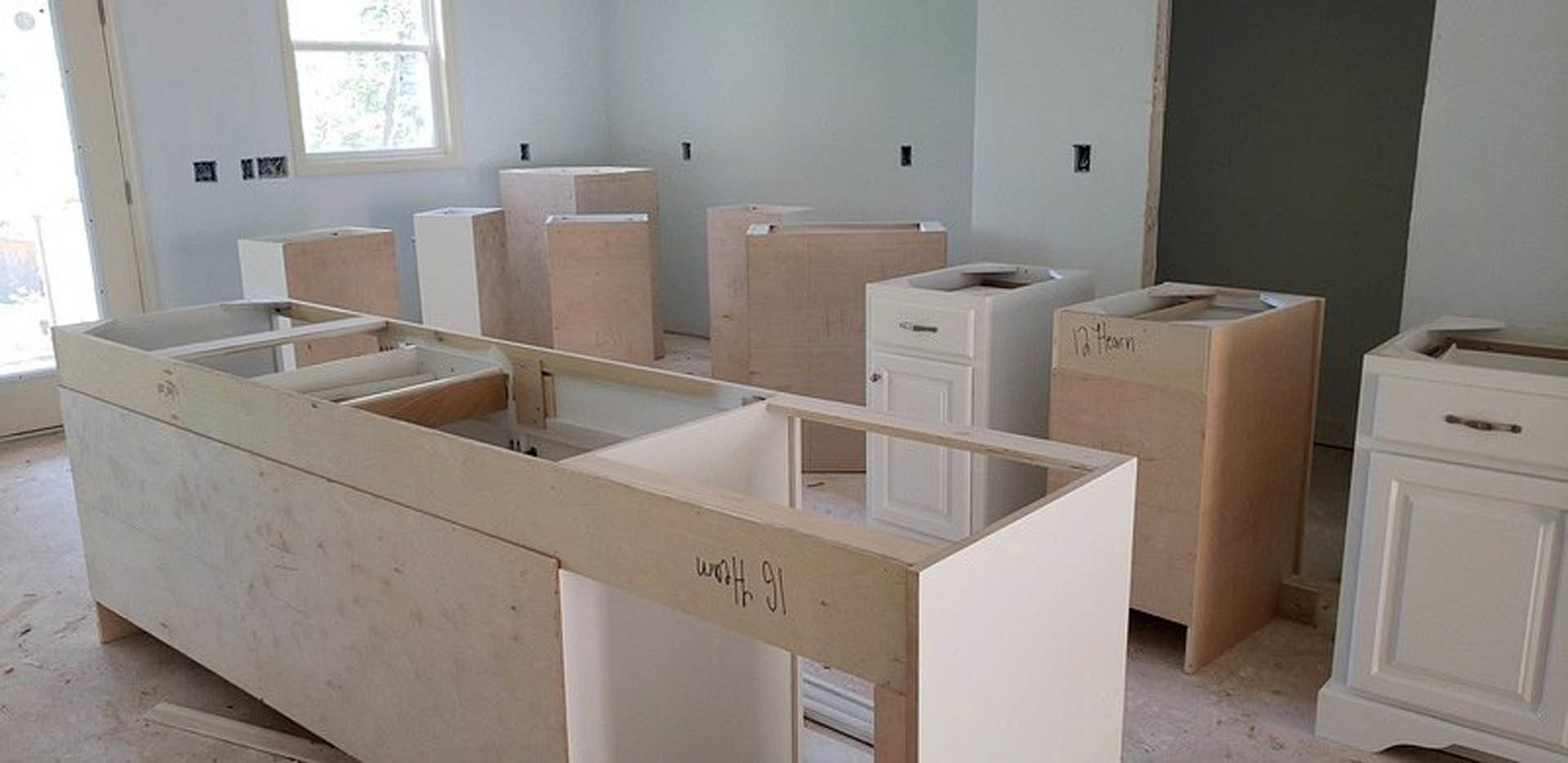 White kitchen with shaker cabinets and drawers, stainless steel sink, stone countertop, window with white trim, light wood flooring