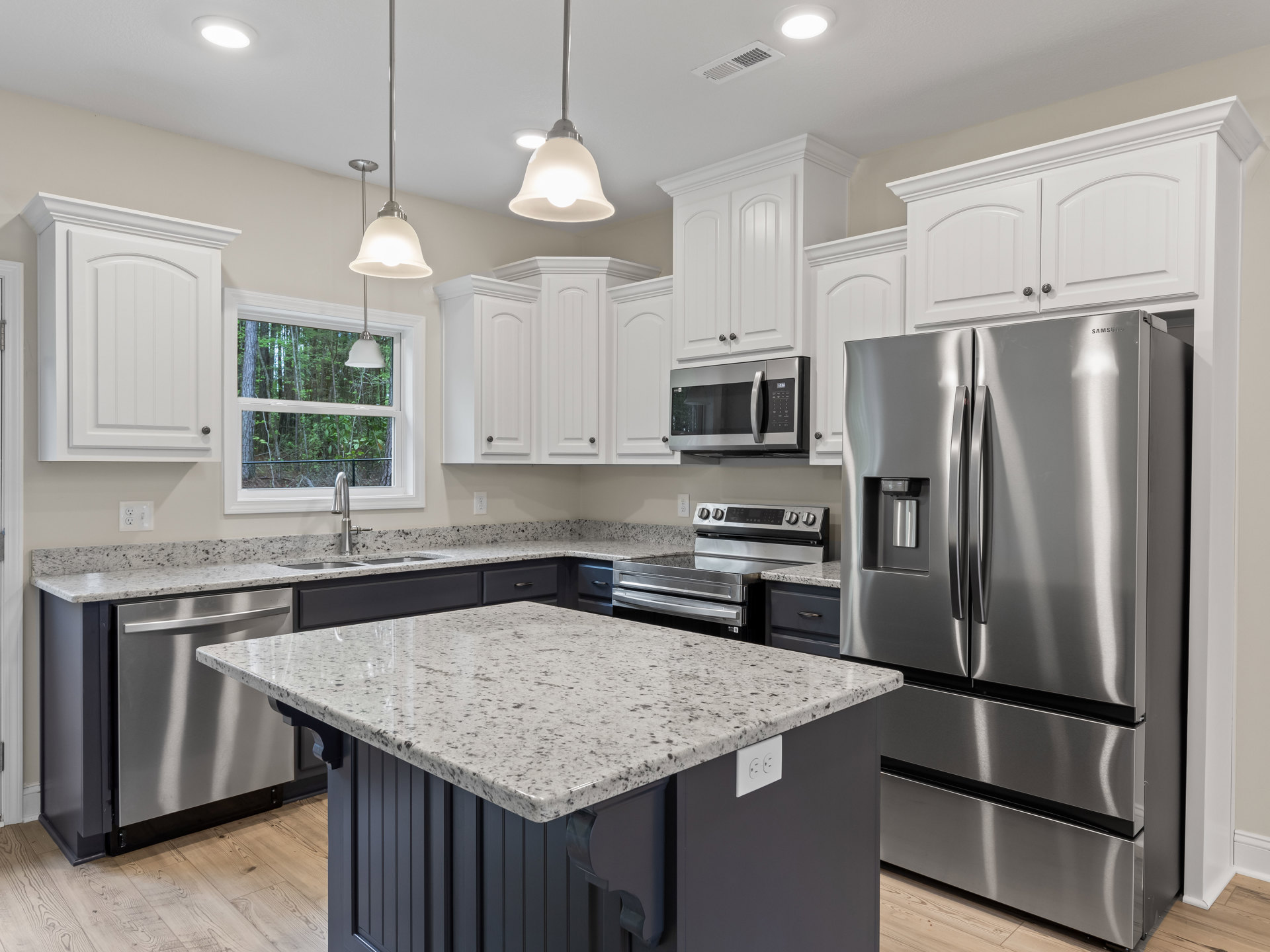 Spacious kitchen featuring a large quartz island, stainless steel refrigerator and oven, built-in microwave, modern pendant light fixture, white cabinetry, and undermount sink with