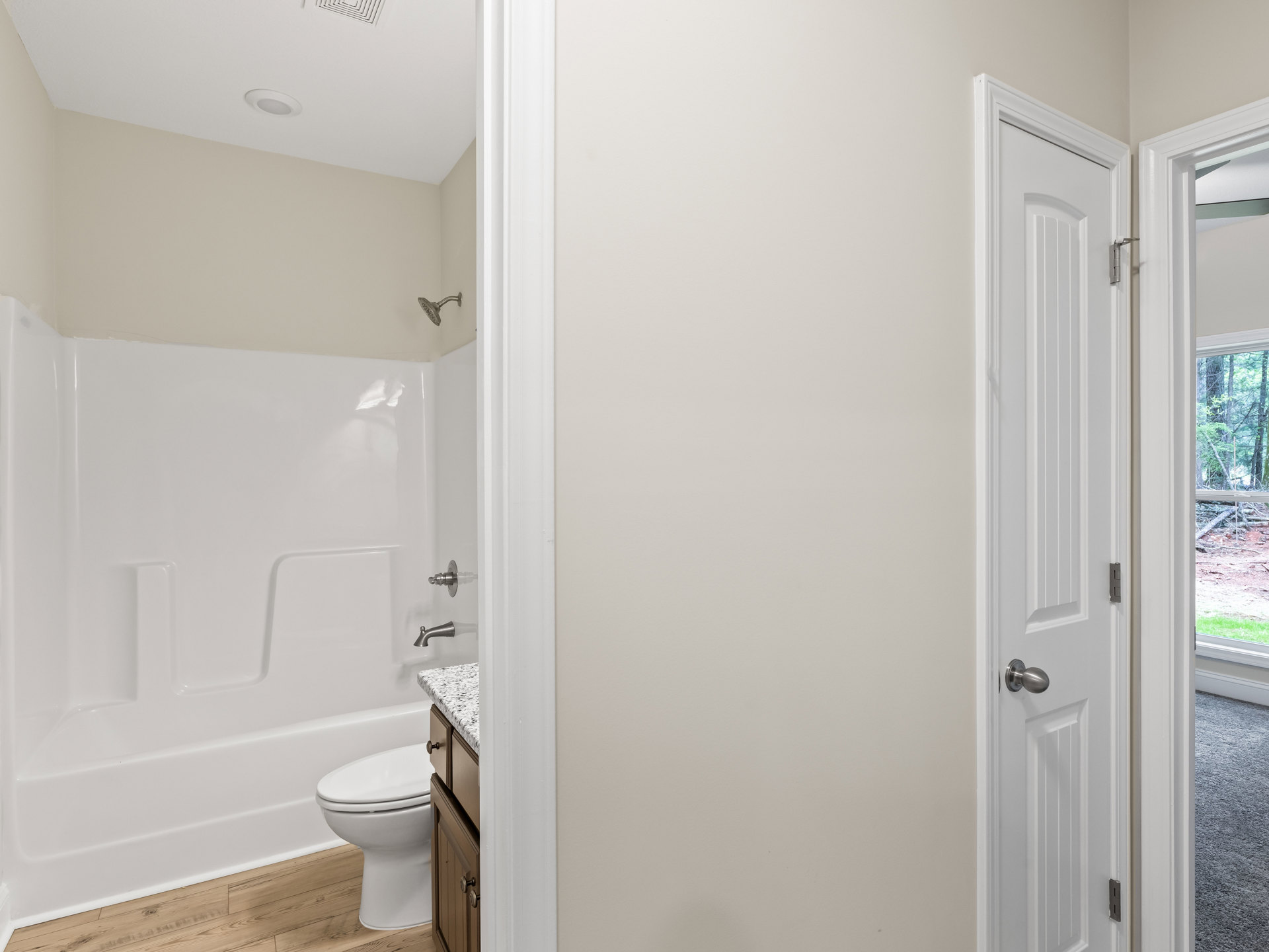 Modern bathroom with white toilet, built-in bathtub, light tile flooring, and a door featuring a metal handle and lock