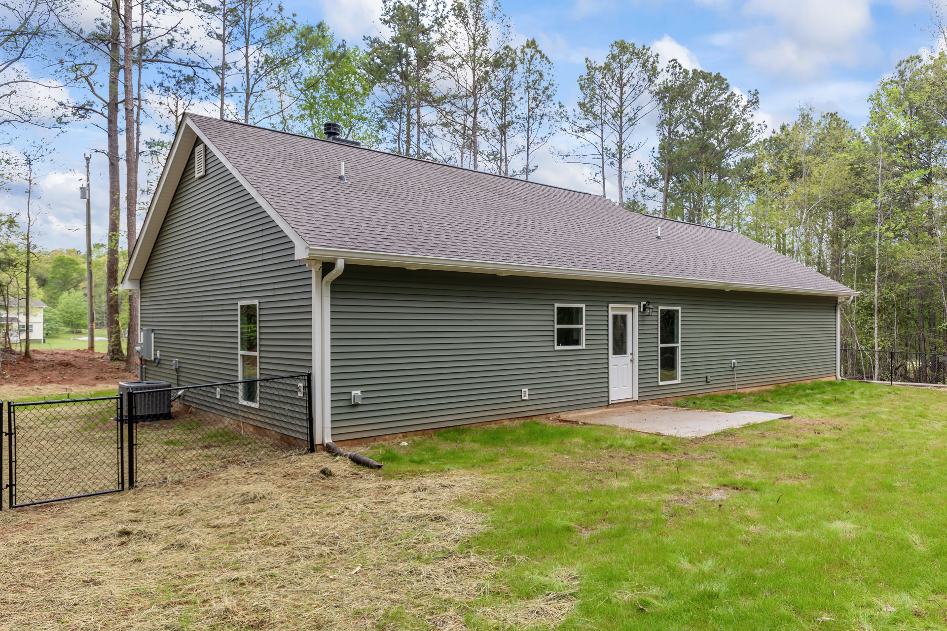 Two-story house with white door and glass panel, white-framed windows, grey shed behind fenced area, green lawn, driveway, mature trees in background, partly cloudy sky
