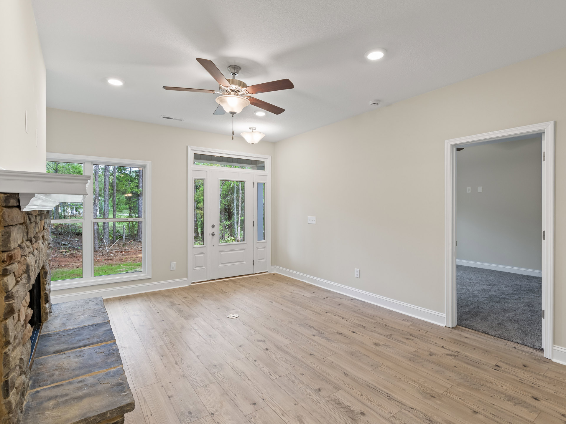 Ceiling fan with light fixture mounted on white ceiling, wood plank flooring, white door with glass panes open to adjacent room, neutral painted walls