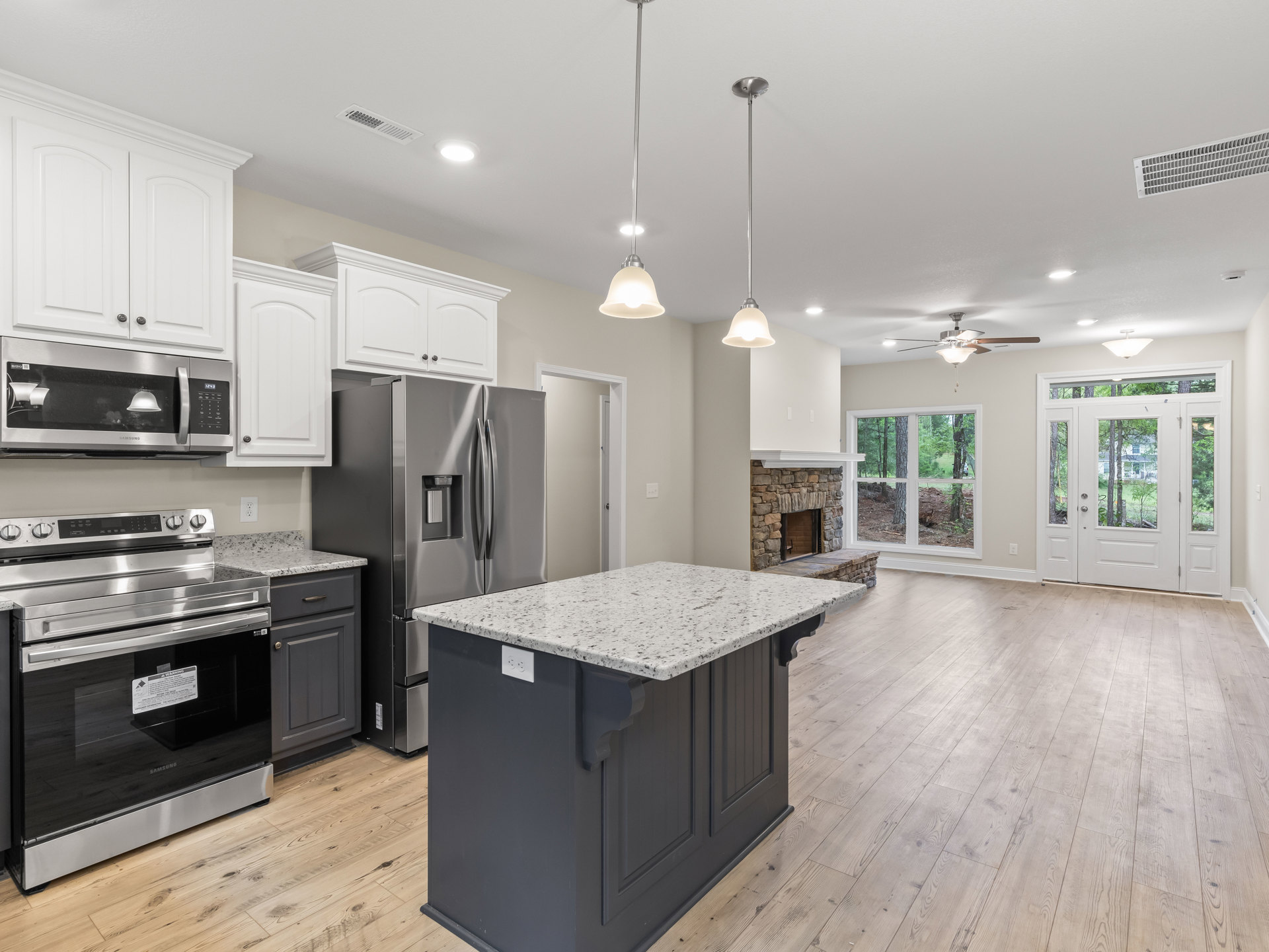 Spacious kitchen featuring a marble-topped island, stainless steel refrigerator, built-in microwave, white cabinetry, and a stone fireplace with wood flooring