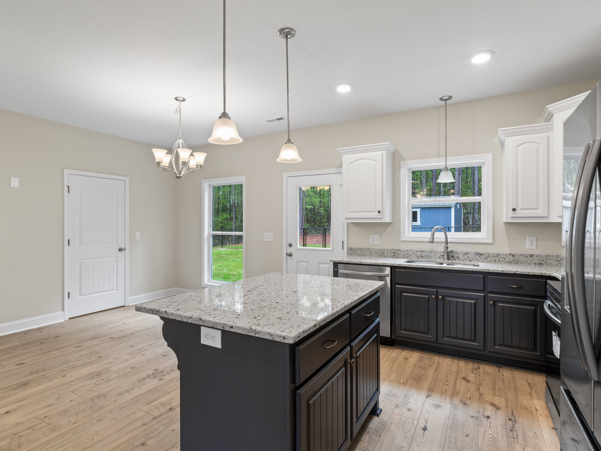 Open kitchen with central marble-topped island, wood flooring, white cabinetry, stainless steel appliances, and silver hardware