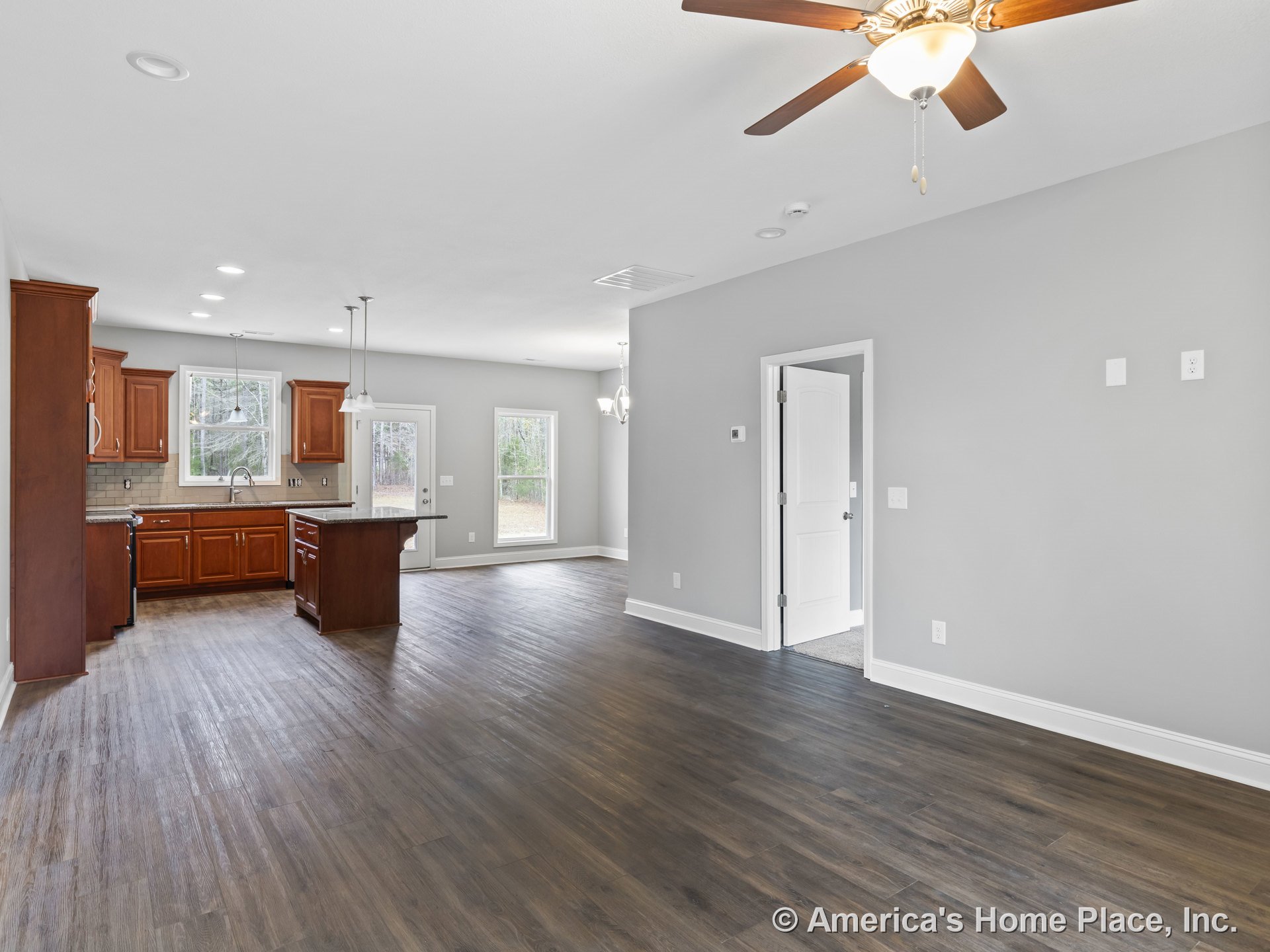 Open concept living area with wood flooring, ceiling fan with light, kitchen featuring wood cabinetry, granite island, tile backsplash, pendant lighting, large windows, and glass