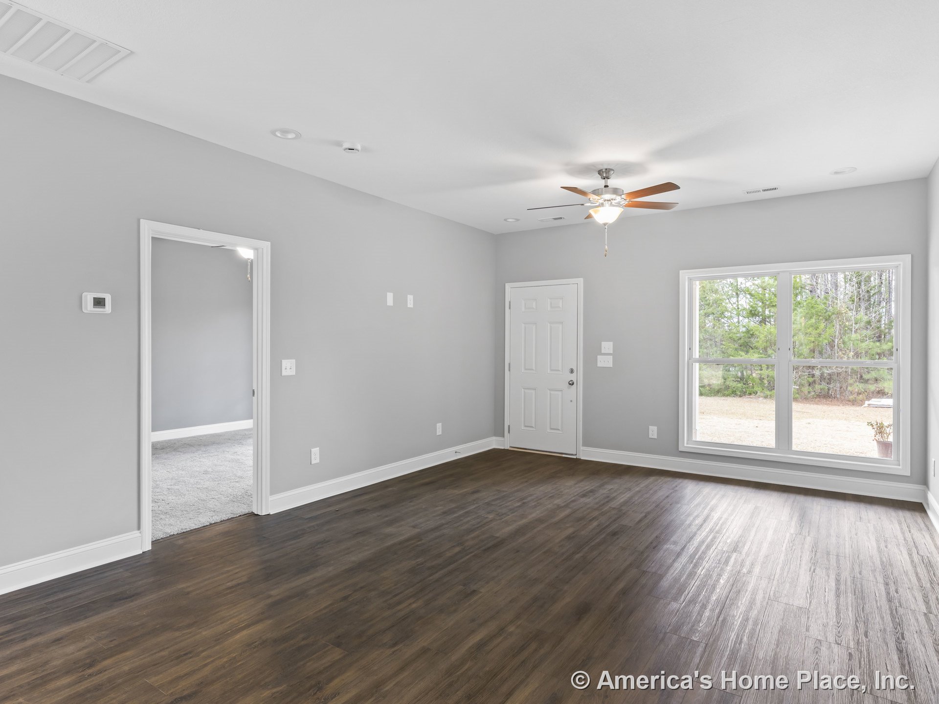 Wide plank wood flooring, large double window allowing natural light, ceiling fan with light fixture, gray painted walls, white trim and baseboards, entry door with access to