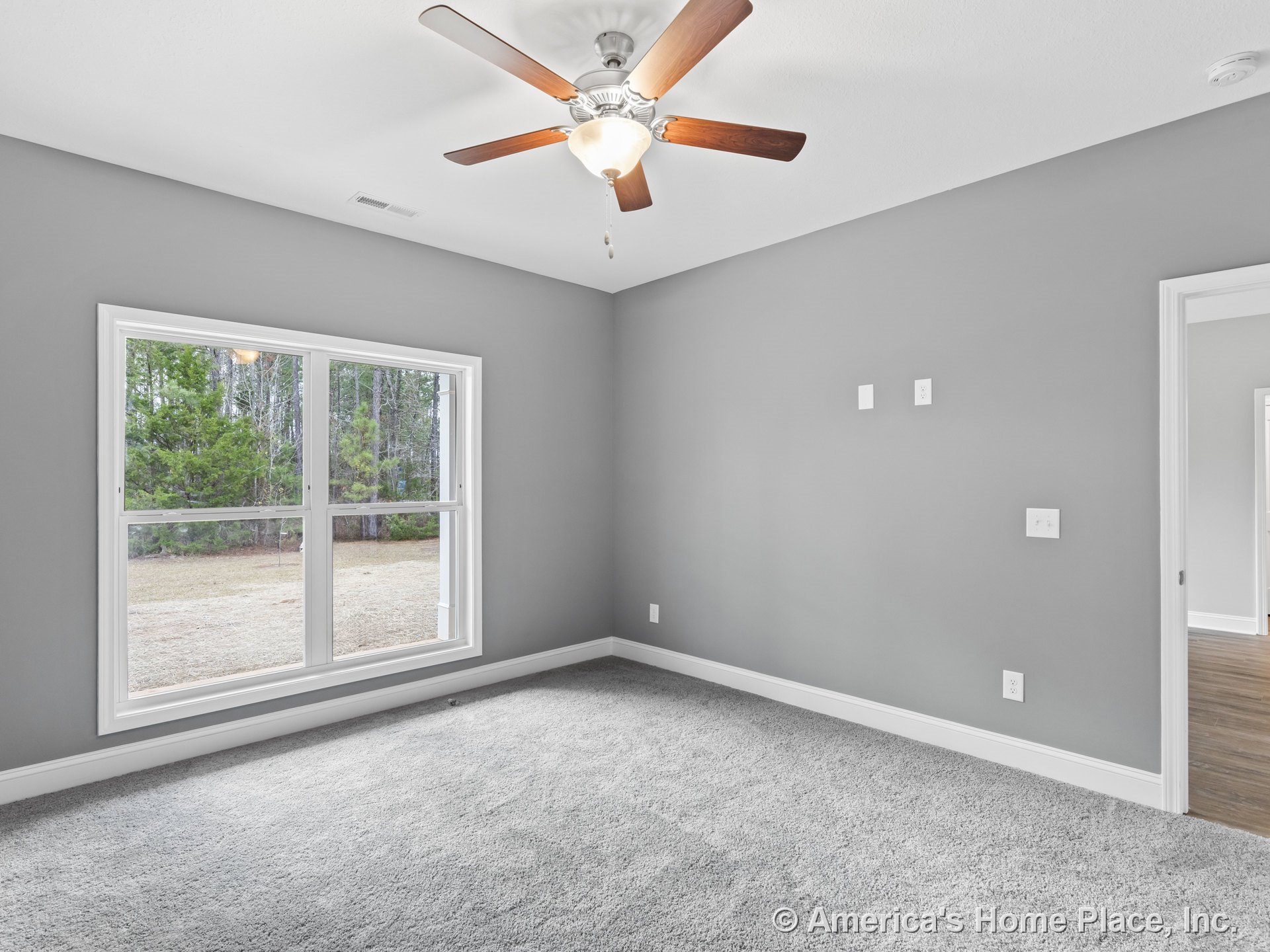 Bedroom with large double window framed in white trim, gray carpet flooring, ceiling fan with integrated light fixture, gray painted walls, white baseboards, visible wall outlets