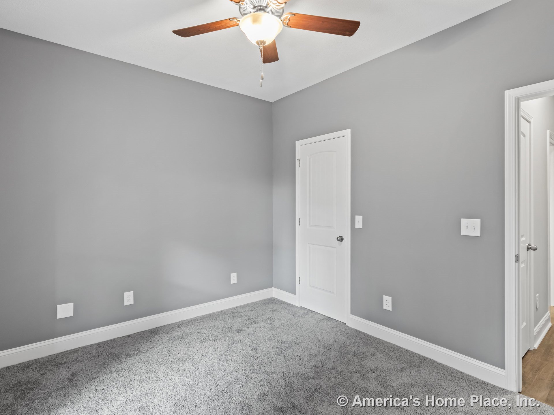 Bedroom with gray walls, white baseboards, carpet flooring, ceiling fan with integrated light, paneled interior door, and multiple electrical outlets.