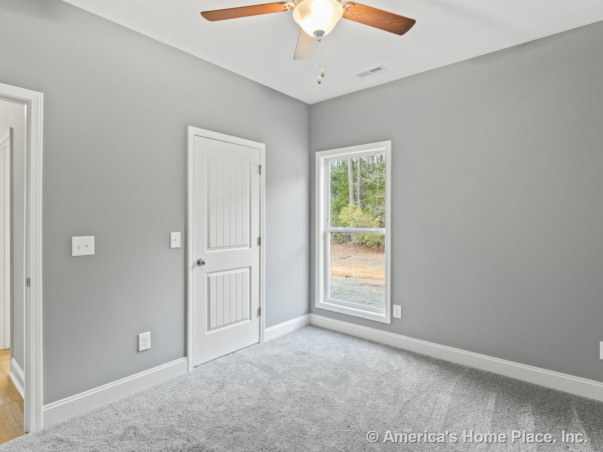 Bedroom with gray carpet flooring, light gray painted walls, white baseboards and door trim, large window with white trim, white paneled interior door, and ceiling fan with light