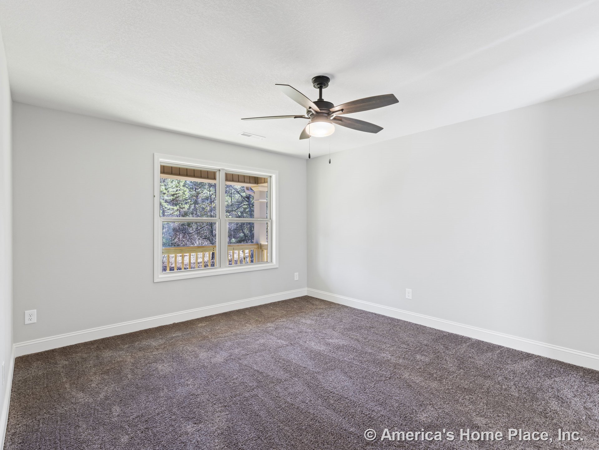 Spacious bedroom with large white-trimmed window overlooking covered porch, ceiling fan with integrated light, neutral walls, brown carpet flooring, and baseboard trim.