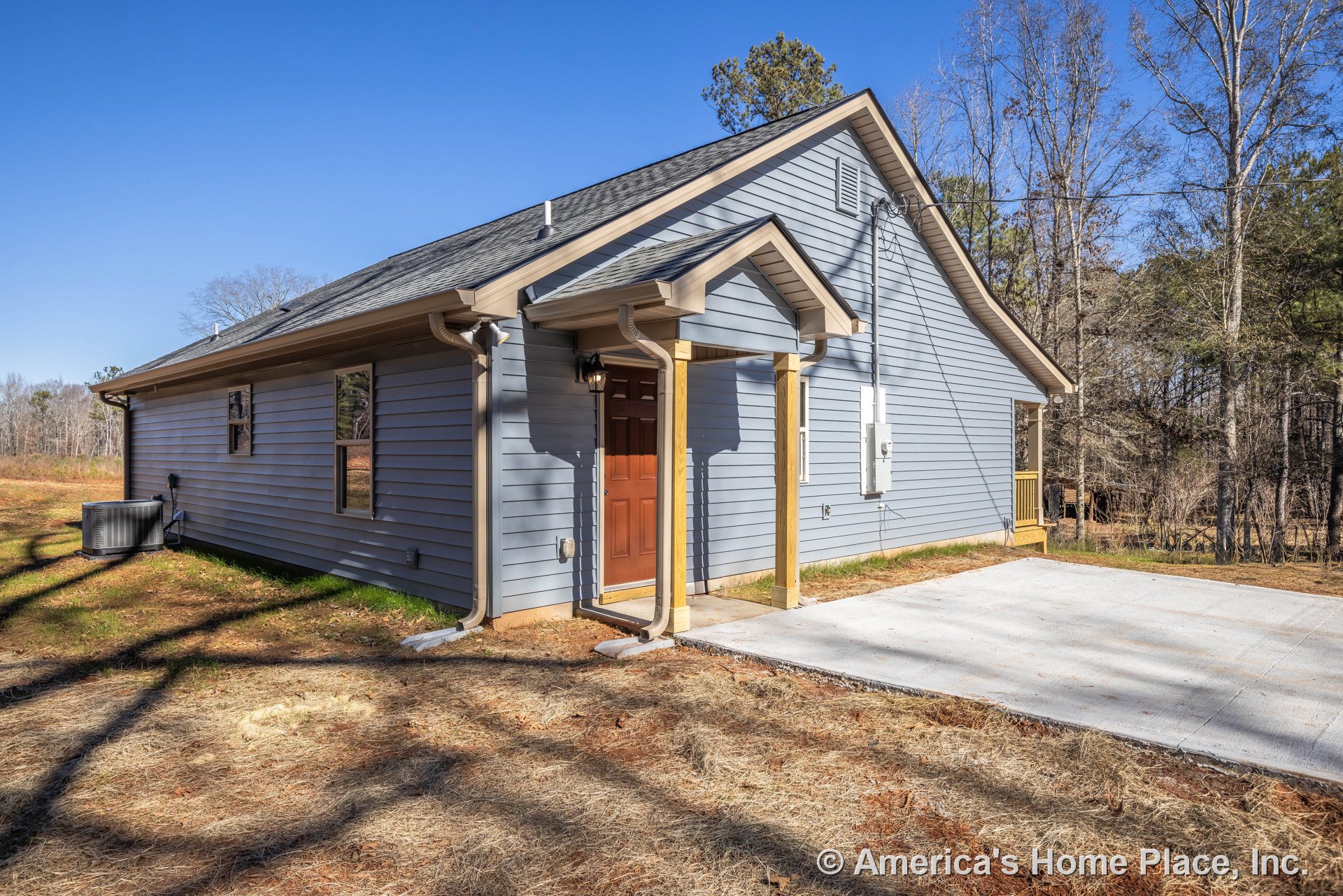 Blue horizontal lap siding with white trim, covered entry porch supported by columns, brown exterior door, concrete driveway, gabled roof with gutters, double-hung windows, visible