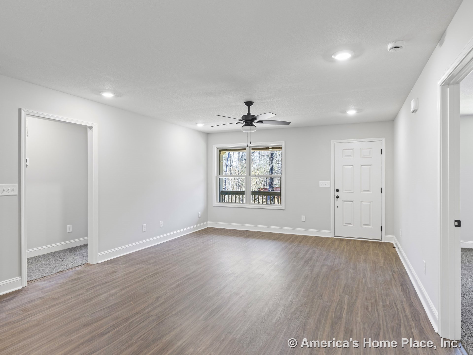 Living room with wood-look plank flooring, white trim and baseboards, recessed ceiling lights, central ceiling fan, double window with exterior view, and white entry door against