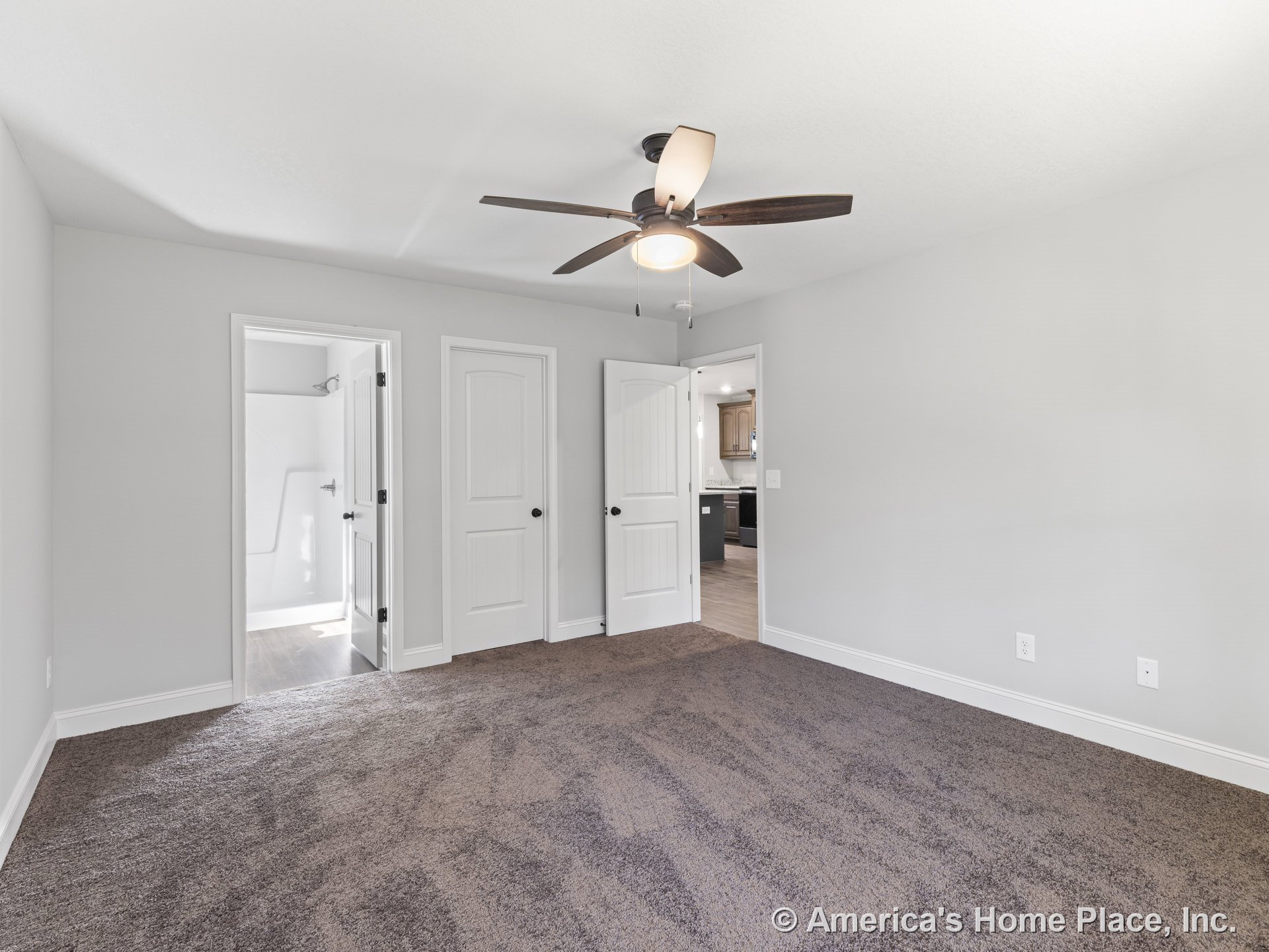 Bedroom with brown carpet flooring, three white paneled doors including closet and bathroom entry, ceiling fan with integrated light, white baseboards, light gray walls, and