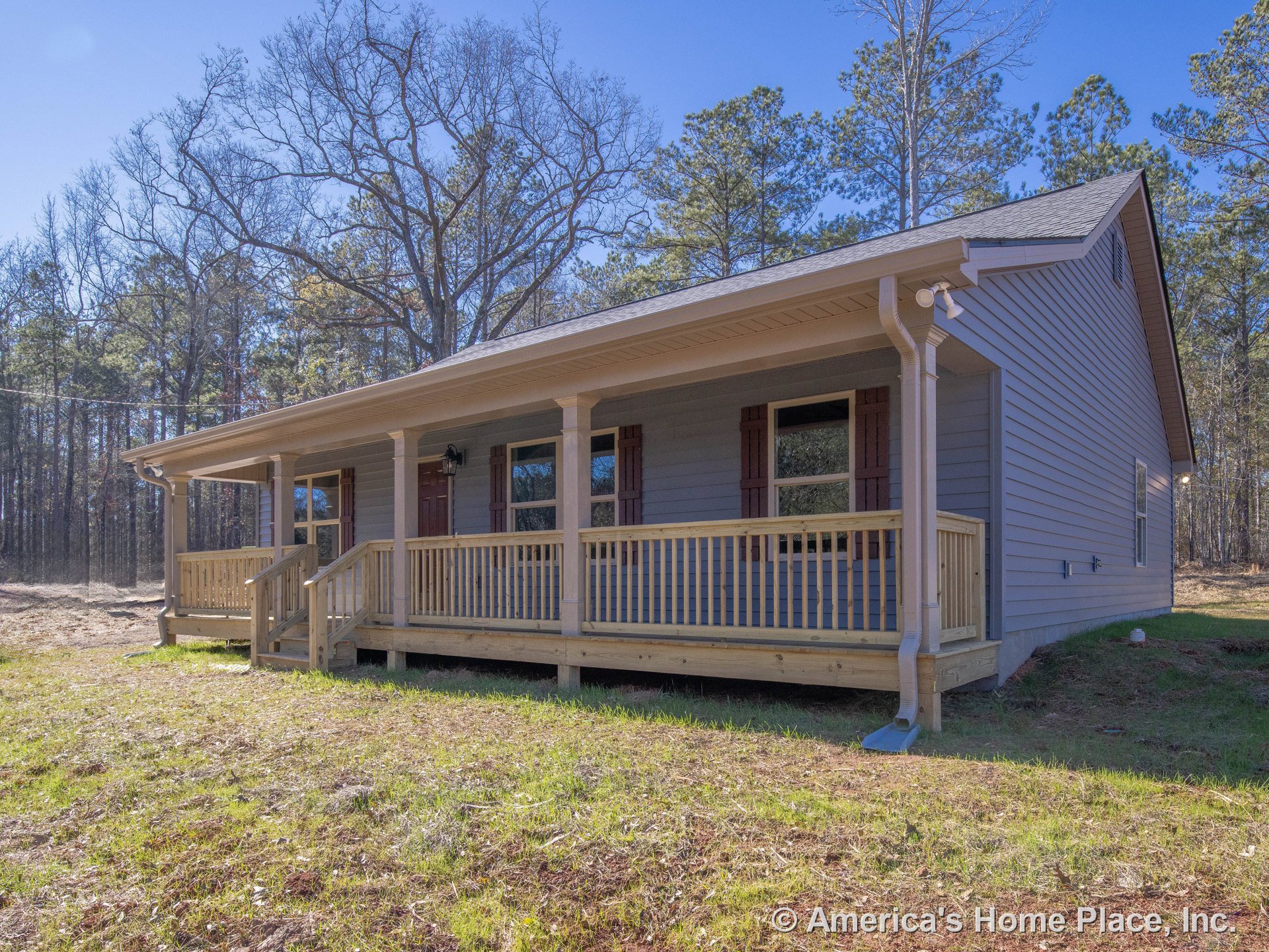 Covered front porch with wood railings and columns, horizontal exterior siding, shuttered windows, front entry door, gutter system along roof edge, rural setting.