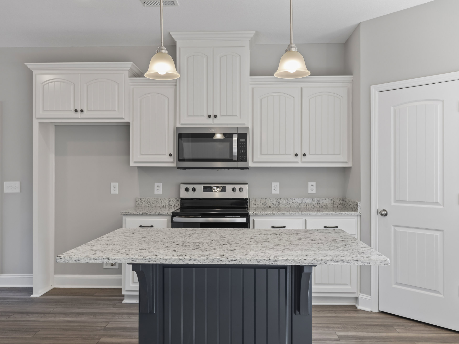 Marble island with waterfall edge, white shaker cabinets, stainless steel stove and microwave, pendant light fixtures, light quartz countertops