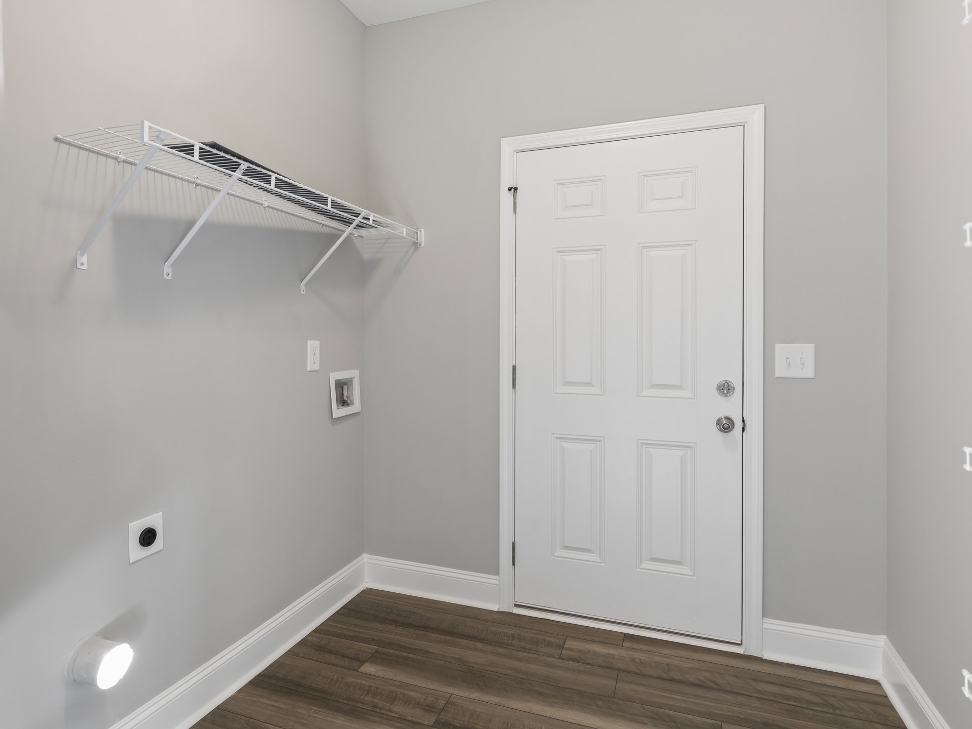 White paneled door with silver knob, white floating shelf mounted on wall, wood flooring, electrical outlet, white plastic utility box with cover, smooth plaster walls and ceiling