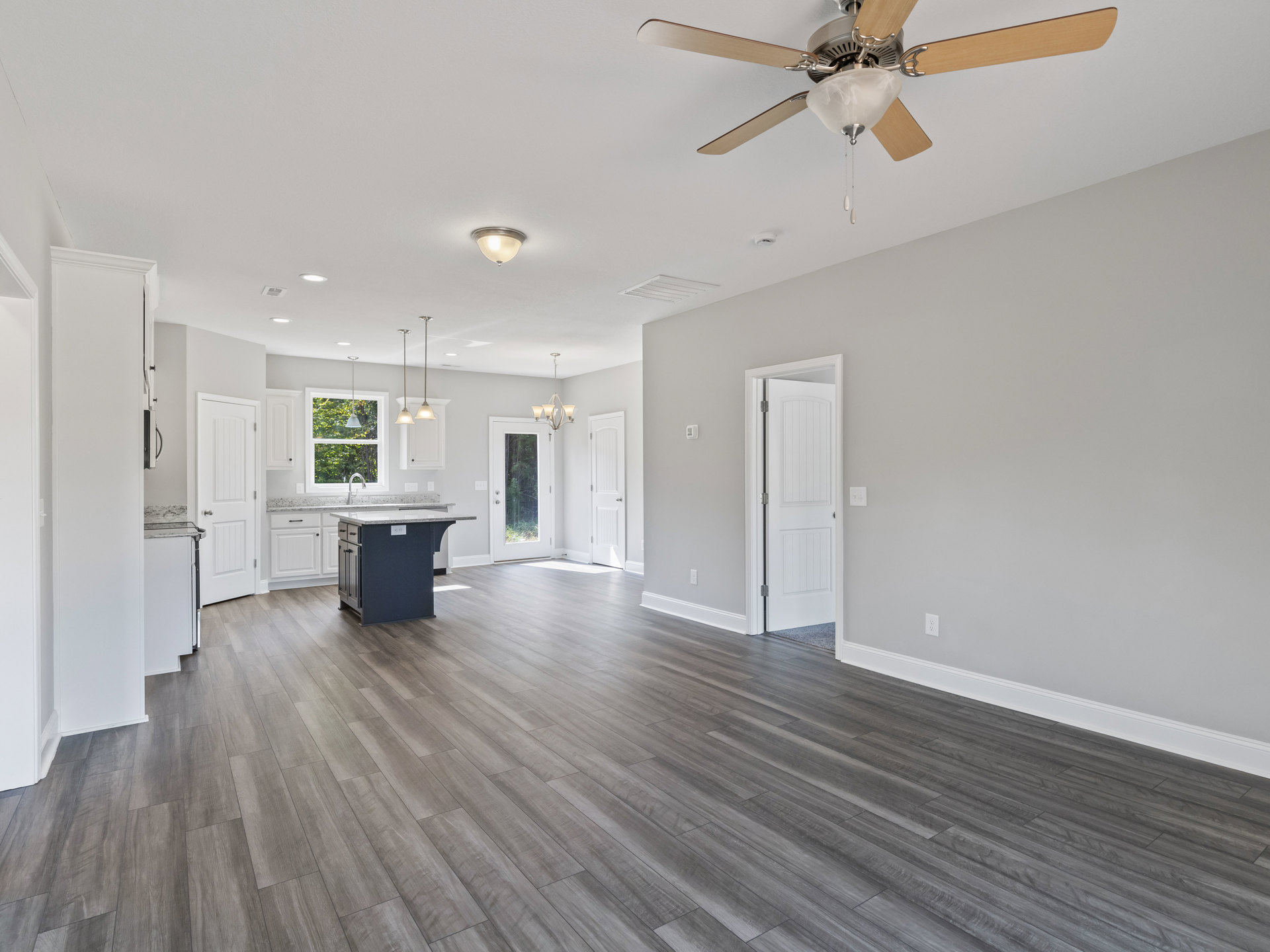 Open-concept kitchen with marble island, hardwood floors, white cabinetry, ceiling fan with light fixture, and white door with black handle