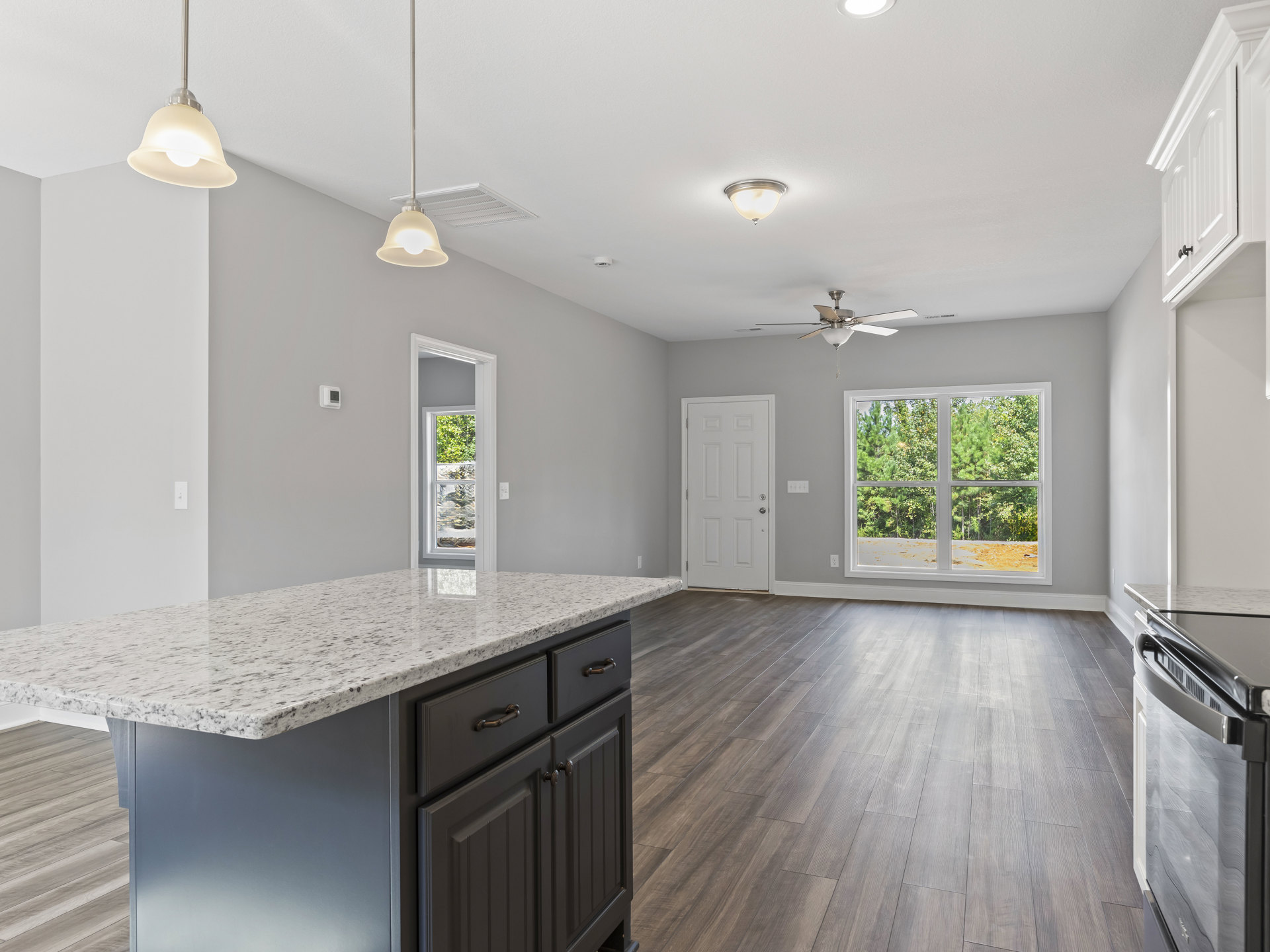 Marble kitchen countertop with hardwood flooring, stainless steel oven, white cabinetry, silver door handle, ceiling light fixture, window overlooking trees, and drawers beneath