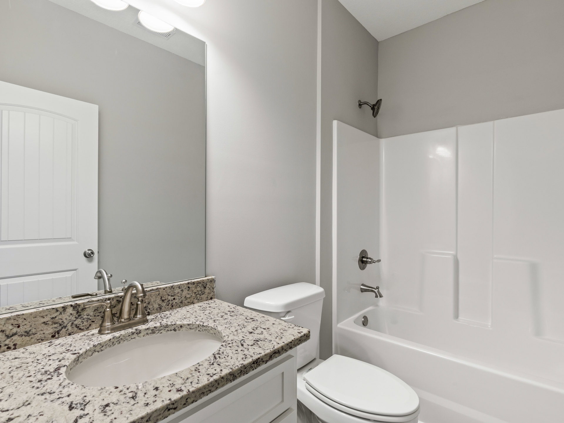Modern bathroom with white porcelain sink and chrome faucet, adjacent toilet with white seat, glass-enclosed shower featuring silver showerhead, light gray tile walls, and white