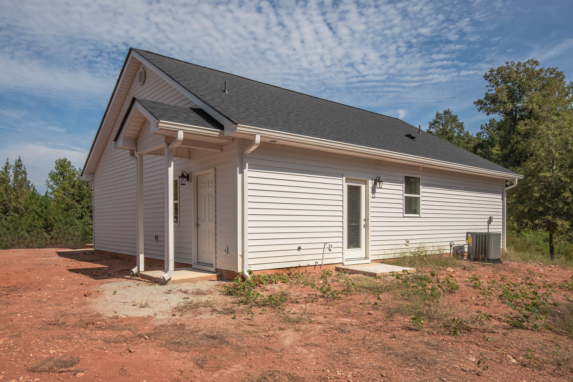 White siding house with black shingle roof, white framed windows, dark front door, trees in background, cloudy sky overhead