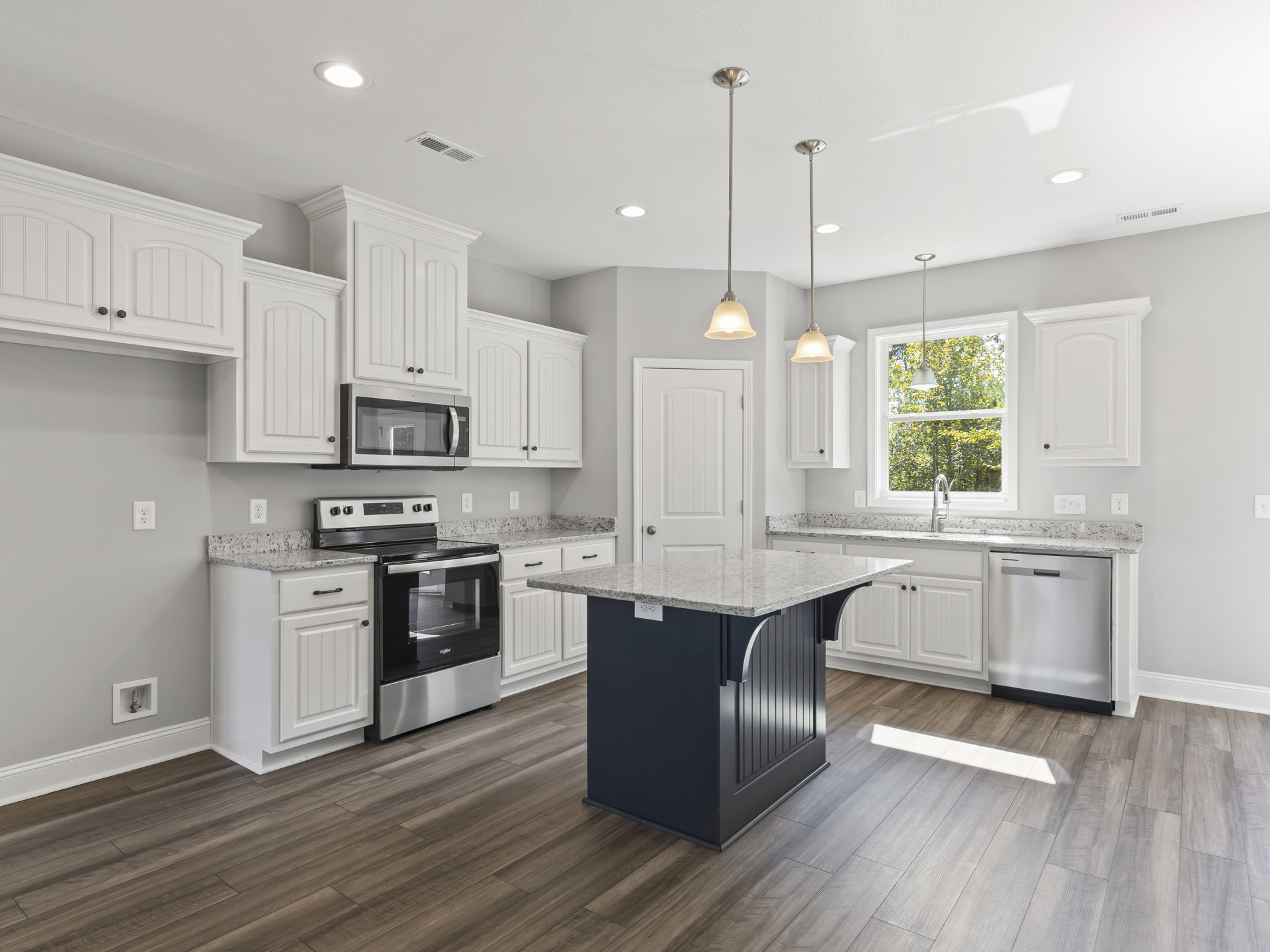White kitchen with marble countertops, central island, stainless steel stove and oven, built-in microwave, white cabinetry, and polished flooring