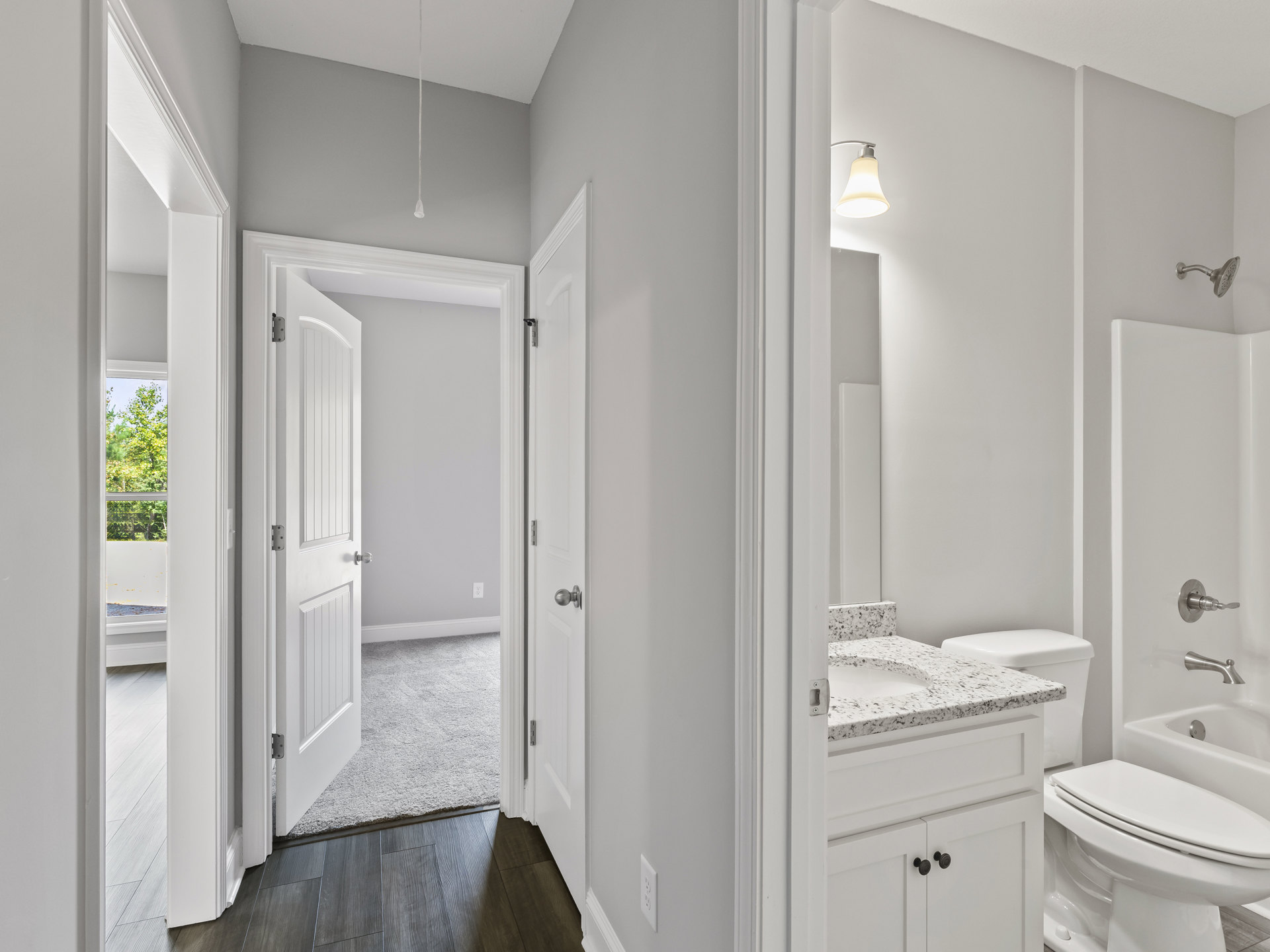 Bathroom with white toilet, white countertop and sink, open door, wall-mounted light fixture, tiled walls, and visible shower head.
