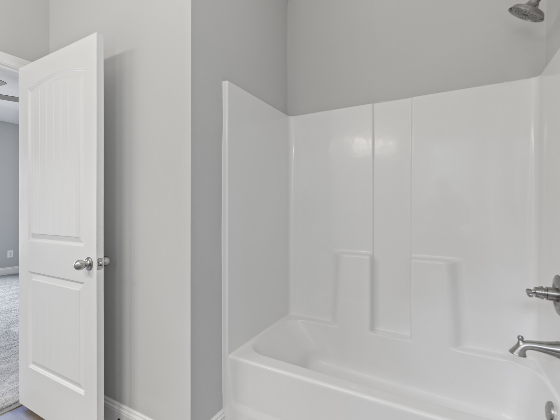 Freestanding white bathtub with chrome faucet set against white tile wall, adjacent to white door with silver knob and minimalist bathroom finishes