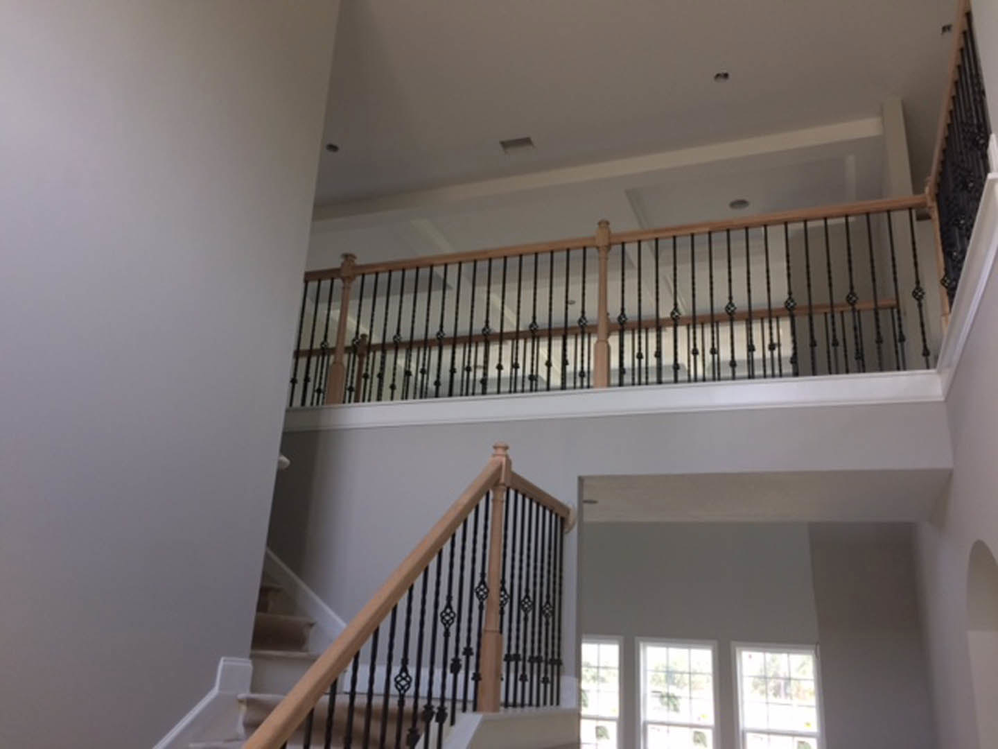Wood staircase with matte black metal railing, white walls, multi-pane window with white trim, crown molding, and plaster finishes